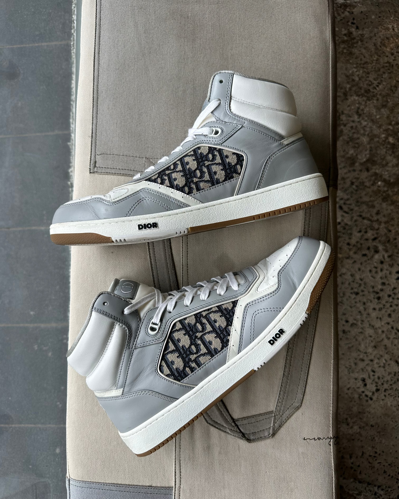 Gray high-top Dior sneaker with black pattern on a gray concrete surface and background