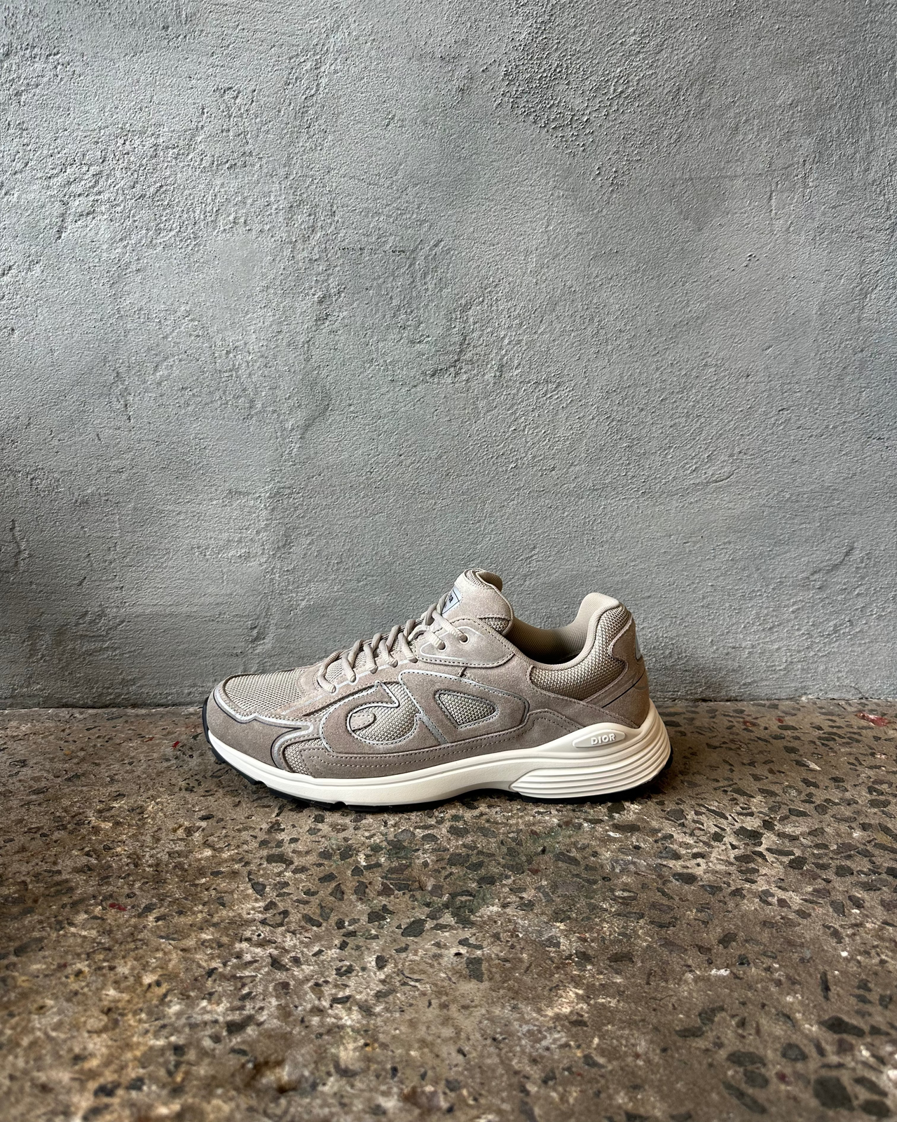 Gray Dior sneaker on a textured concrete floor against a gray wall