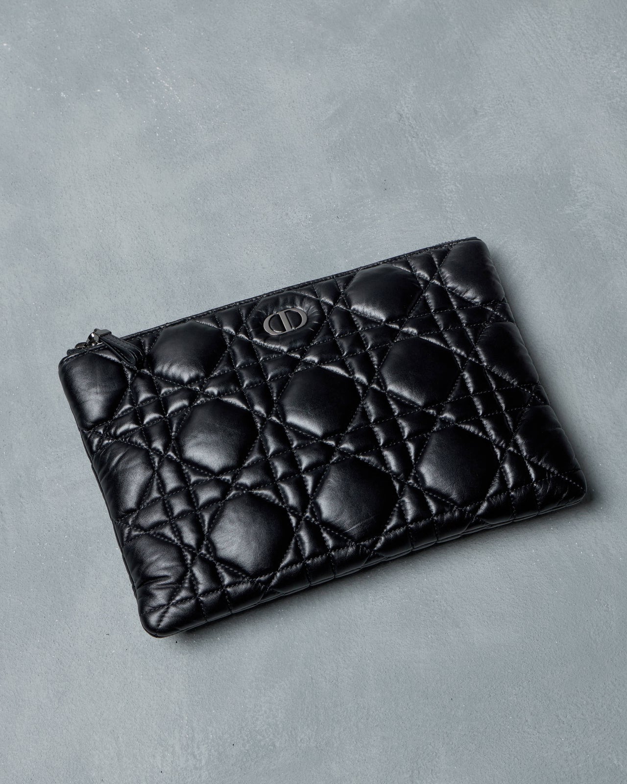 Black quilted Dior leather pouch on a gray background
