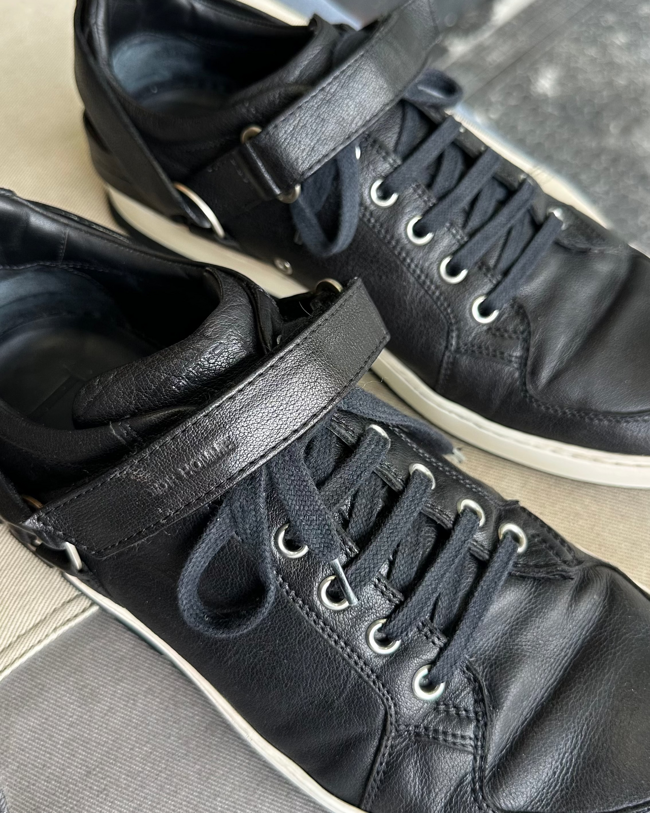 Black Dior Homme sneaker on a gray surface with a gray background