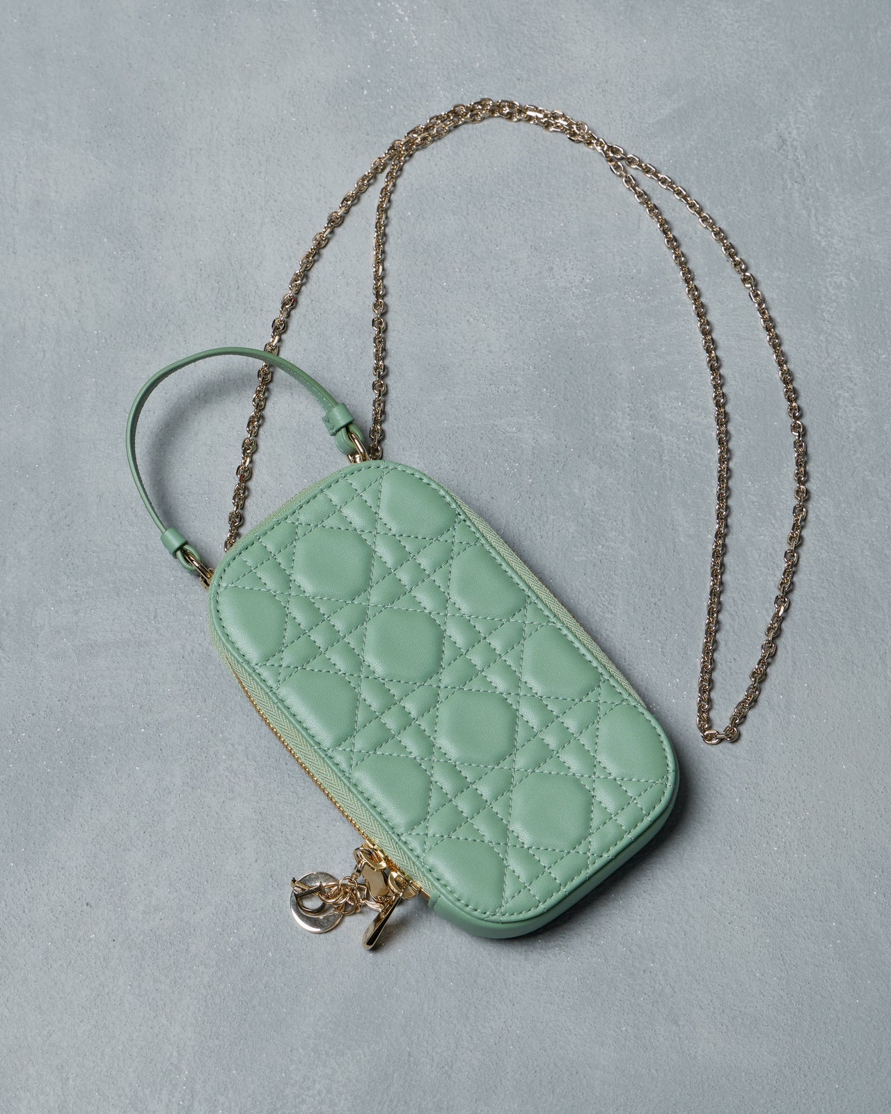 Mint green quilted Dior phone case with gold charm on a gray background