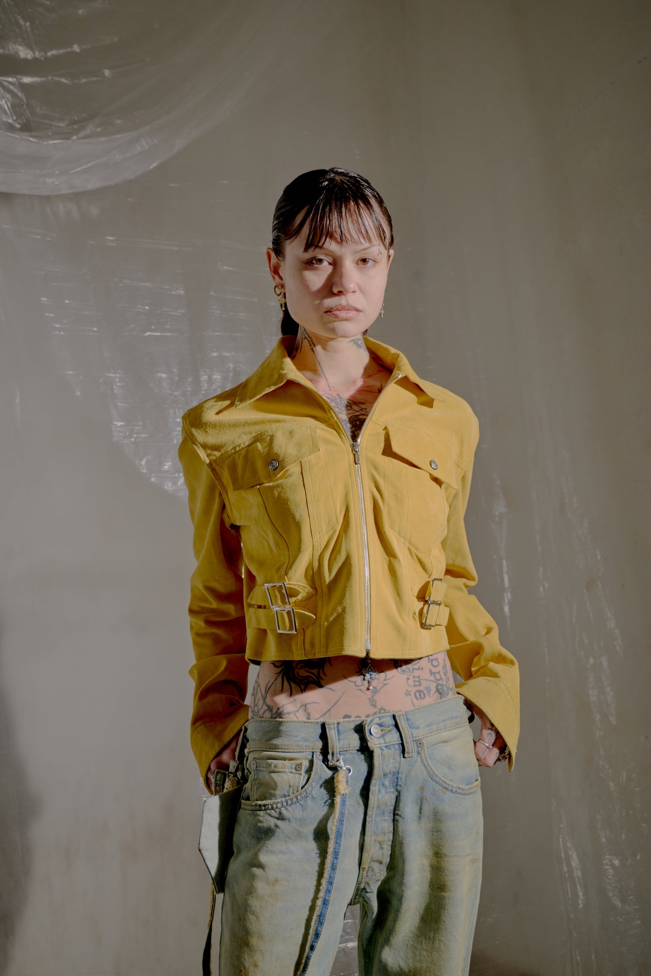 Young person in a yellow Dior jacket and jeans. The backdrop features translucent drapery.