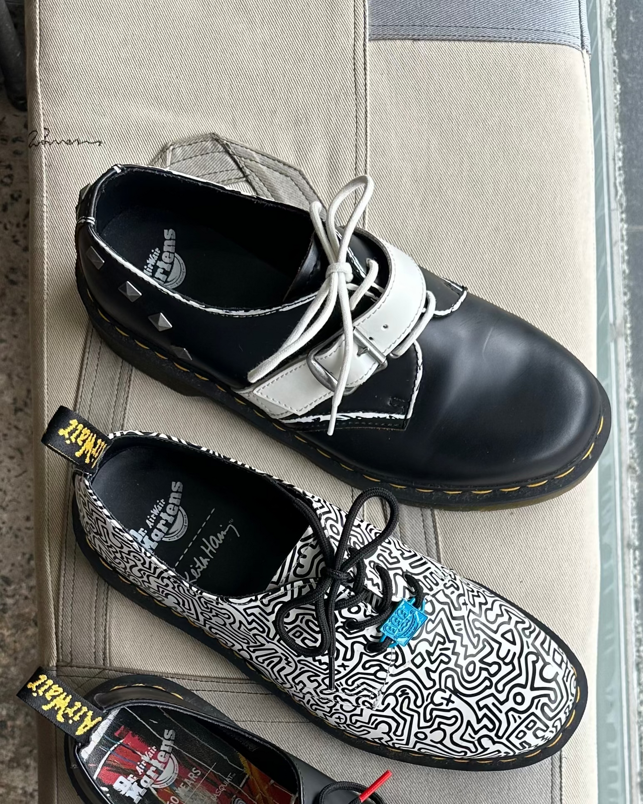 Black leather doc martens shoe with white laces on a textured surface and gray wall background