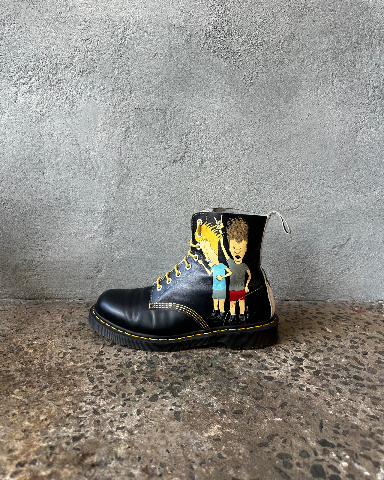 Black doc martens boot with colorful graphic design on a textured surface and gray background