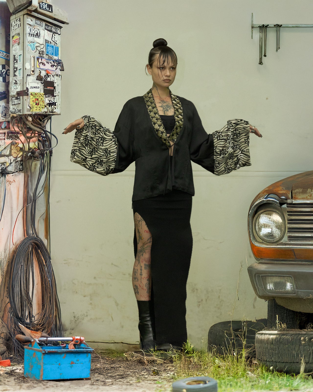A person standing in a garage wearing a black beaded Dries Van Noten kimono with fuzzy floral details, displaying the garment's sleeve and collar.