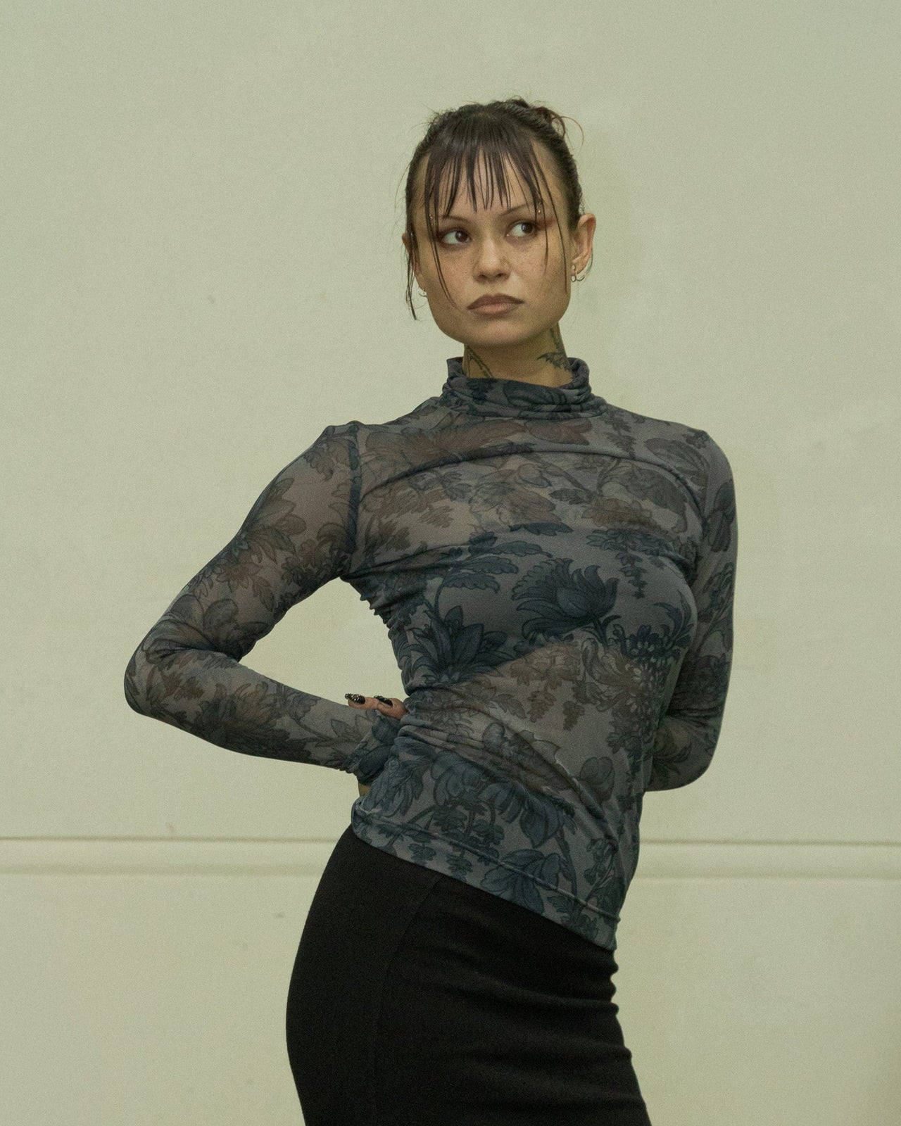 A person wearing a floral Dries Van Noten turtleneck long-sleeve top in a dilapidated room with books and debris around.