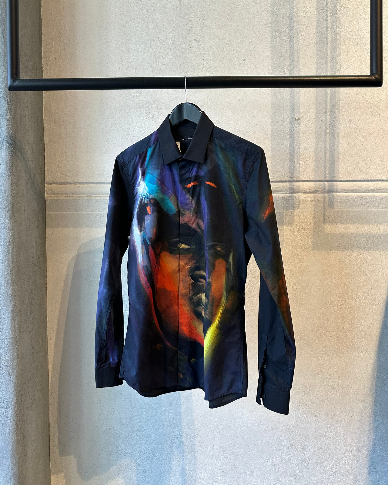 Colorful Givenchy shirt with artistic design of a face on a hanger against a neutral background