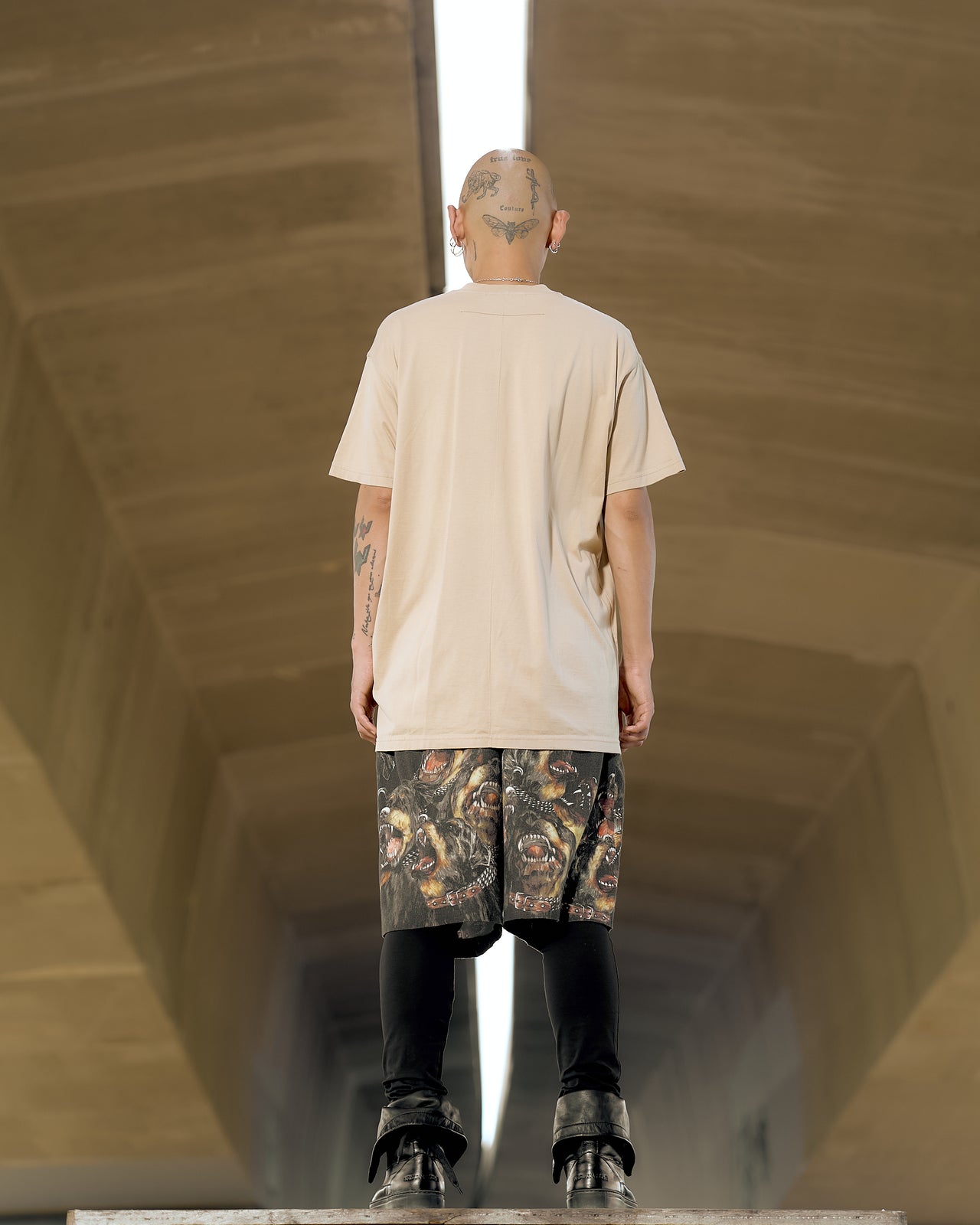 A male model wearing a beige Givenchy t-shirt with a graphic mandala print of chains, studs, stars, and snarling dogs.