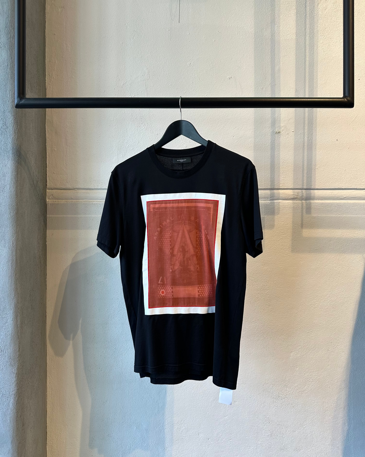 Black Givenchy t-shirt with a red and white graphic on a hanger against a neutral wall.