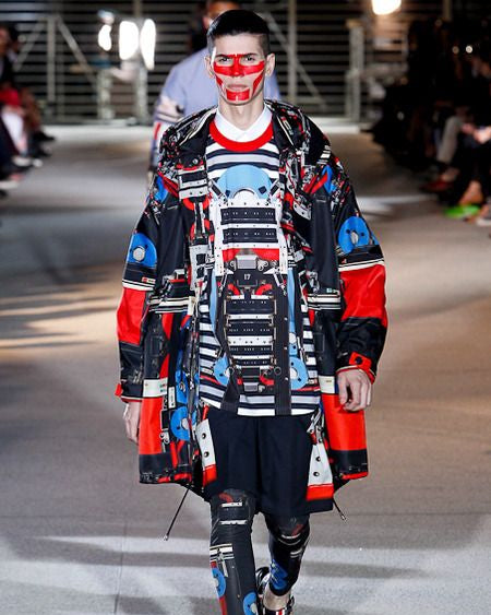Model on a Givenchy runway wearing a colorful outfit with red, blue, and black patterns.