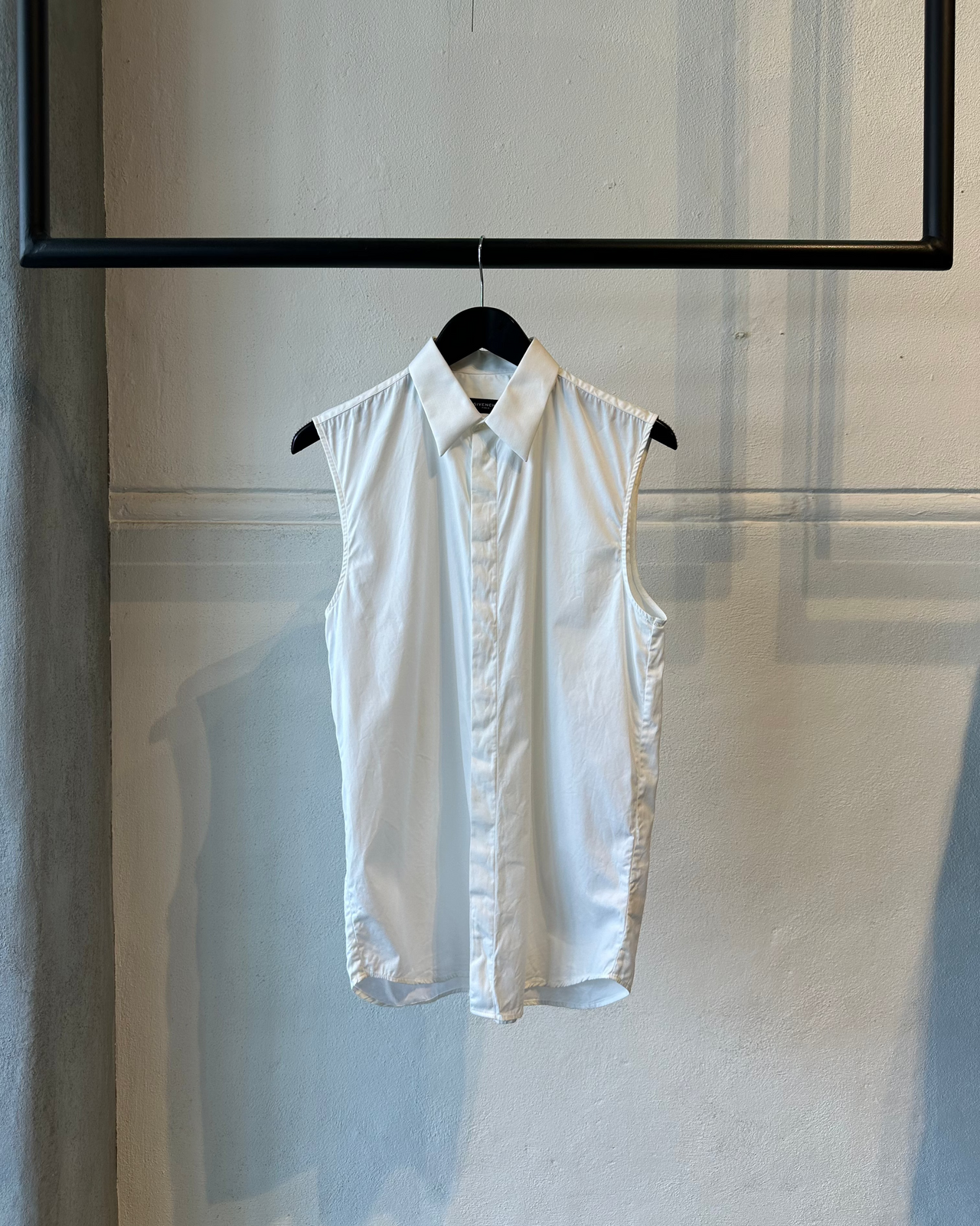 White sleeveless Givenchy shirt on a hanger against a light-colored wall.
