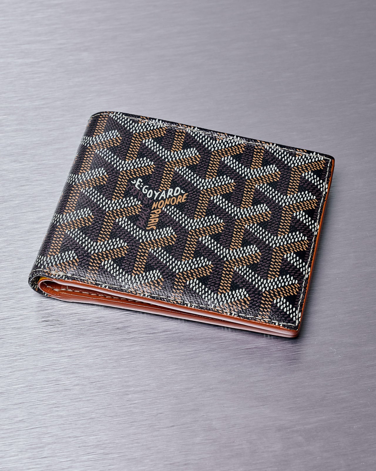 A black and brown Goyard Victoire wallet with a geometric pattern, constructed from hand-painted Goyardine canvas, shown closed.