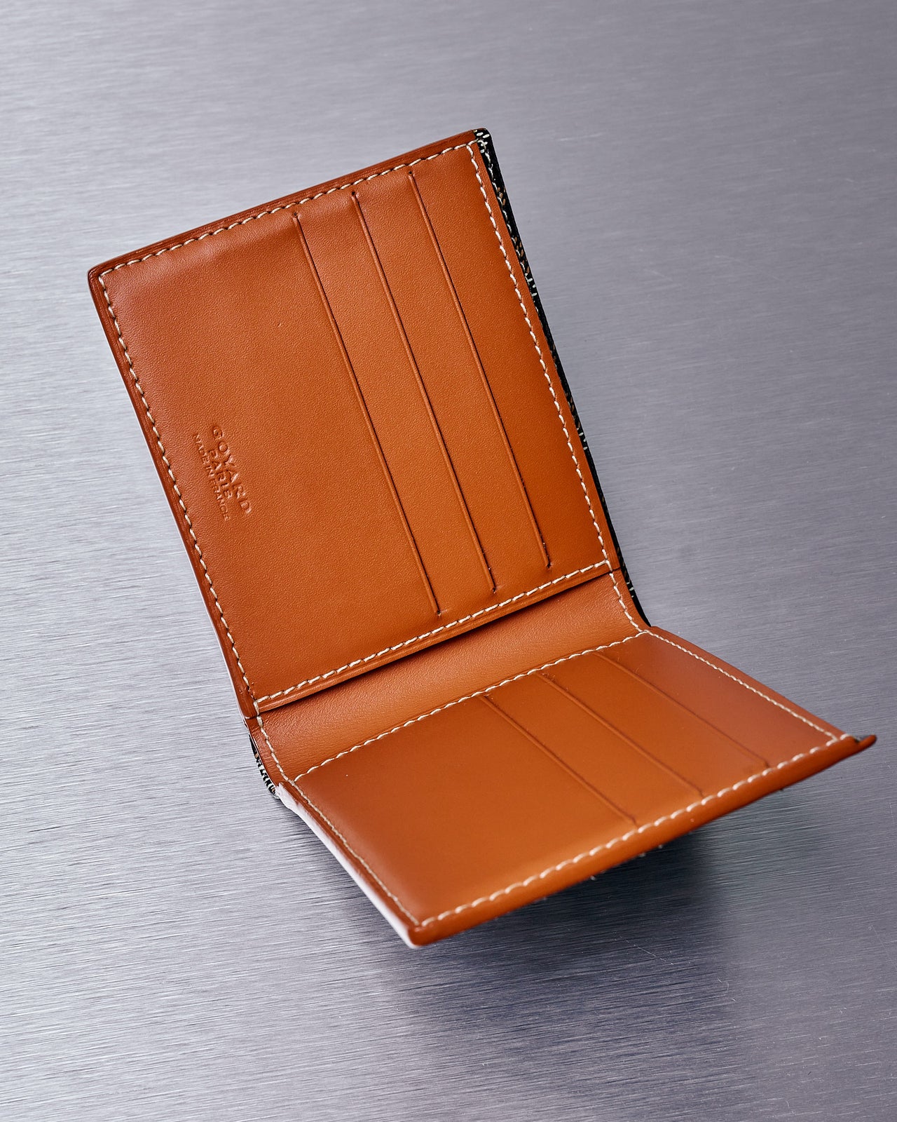 A black and brown Goyard Victoire wallet with a geometric pattern, constructed from hand-painted Goyardine canvas, shown closed.