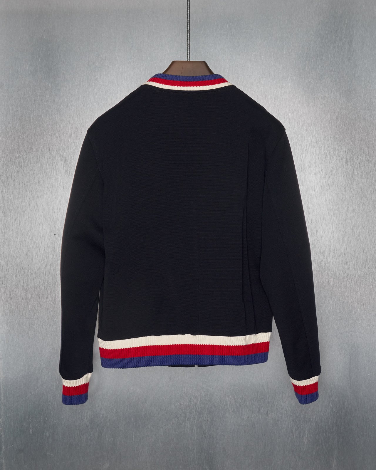 A black Gucci zip-up bomber jacket with a red and white striped trim on the collar, cuffs, and hem. Features a red and white patch in the shape of a panther on the front.
