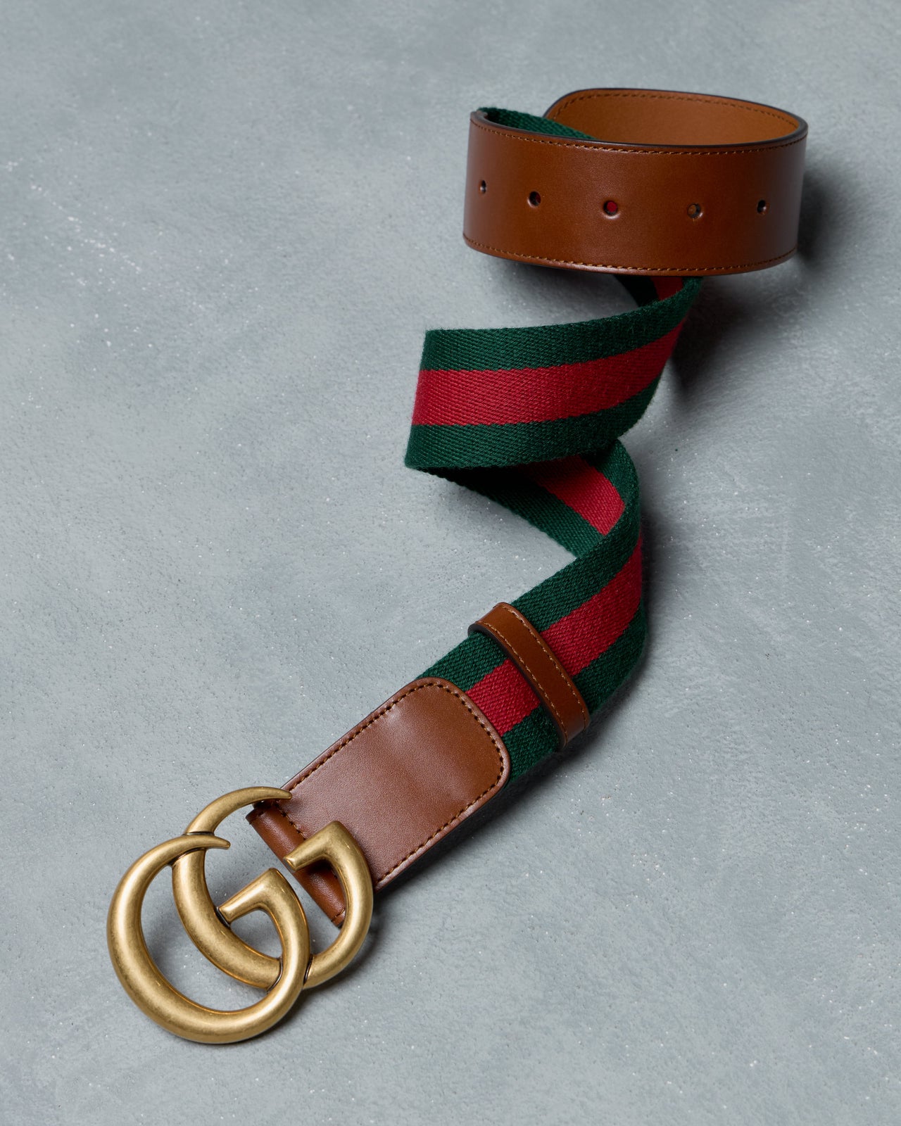 Gucci belt with green and red striped strap and brown leather buckle on a gray background