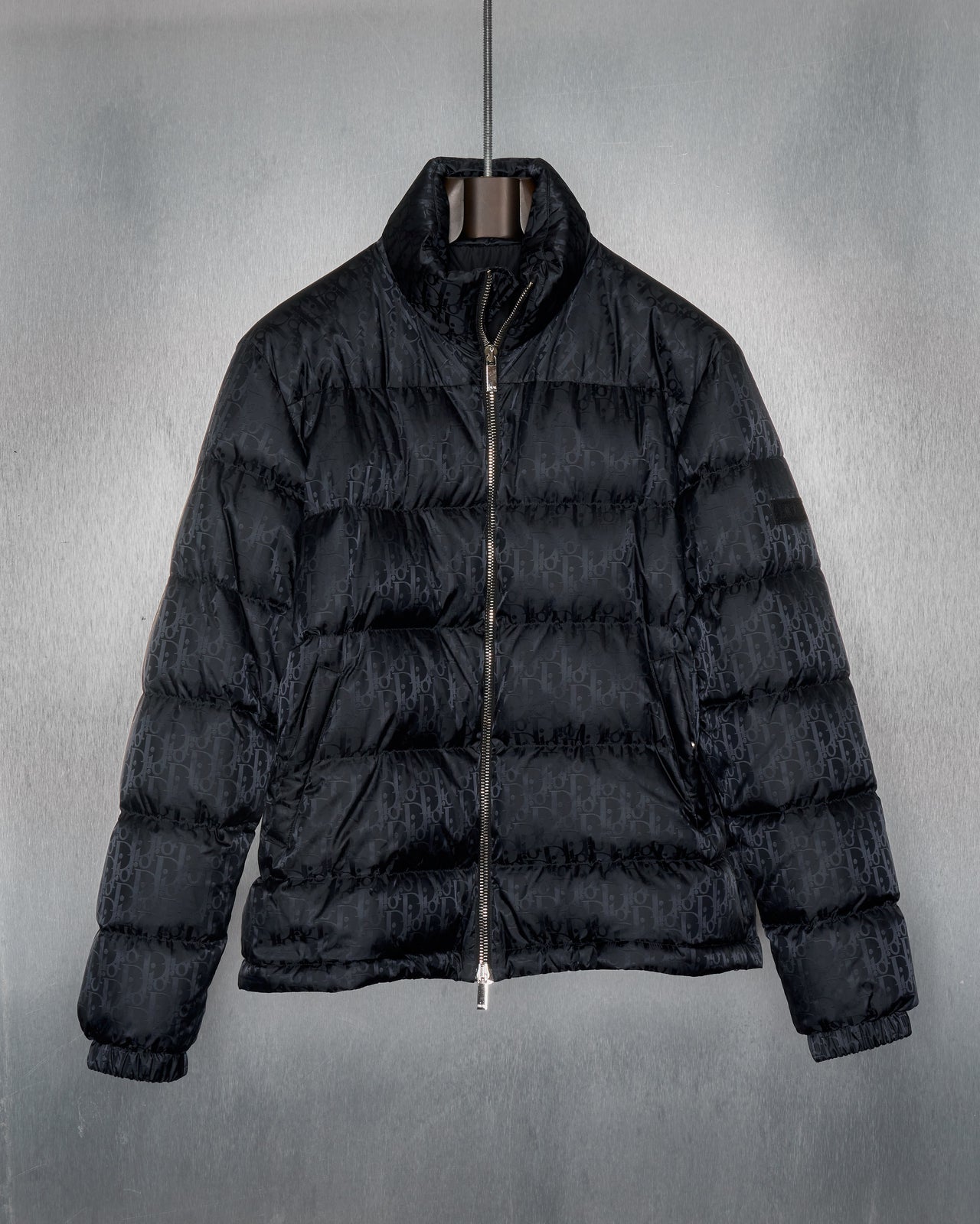 A black Dior 2019 Oblique technical jacquard down jacket displayed against a textured background.