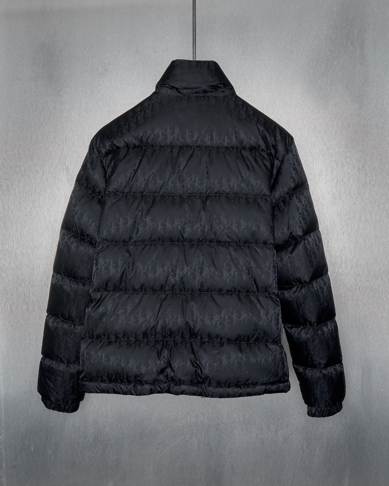 A black Dior 2019 Oblique technical jacquard down jacket displayed against a textured background.