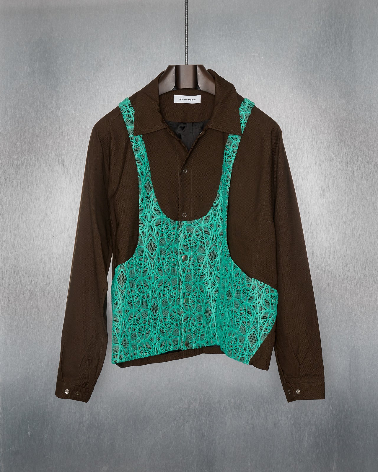 Person wearing a brown Kiko Kostadinov outfit with a teal patterned top, standing in front of a green wall with a giraffe graphic.