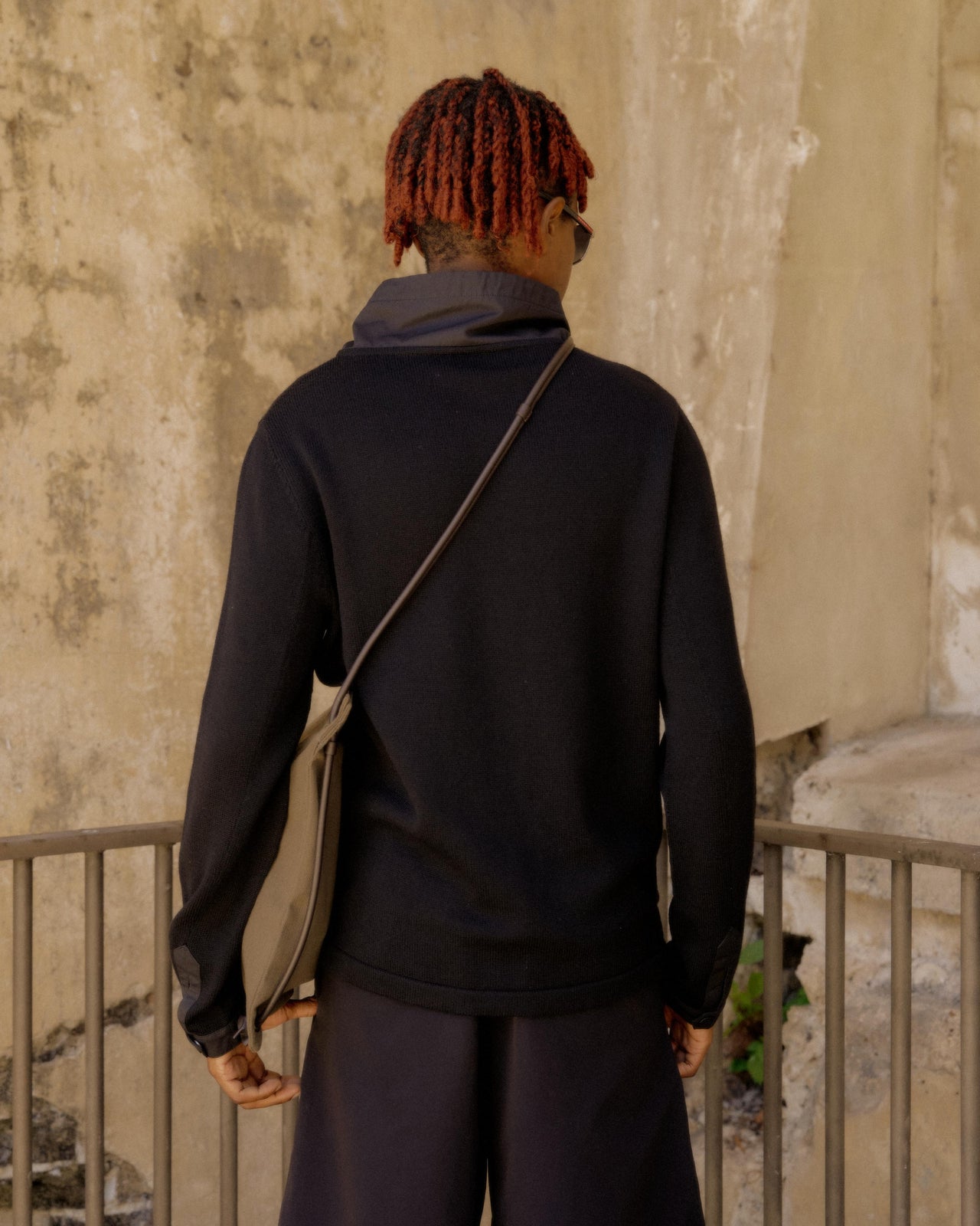A person in a black Hermès hoodie and shorts leans against a textured wall.