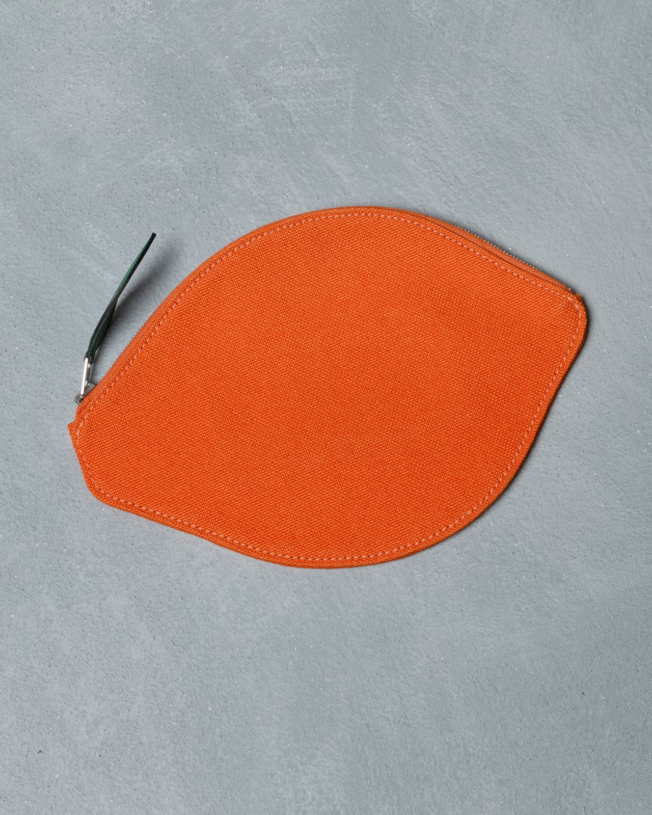 Orange fabric Hermès pouch with a zipper on a gray background