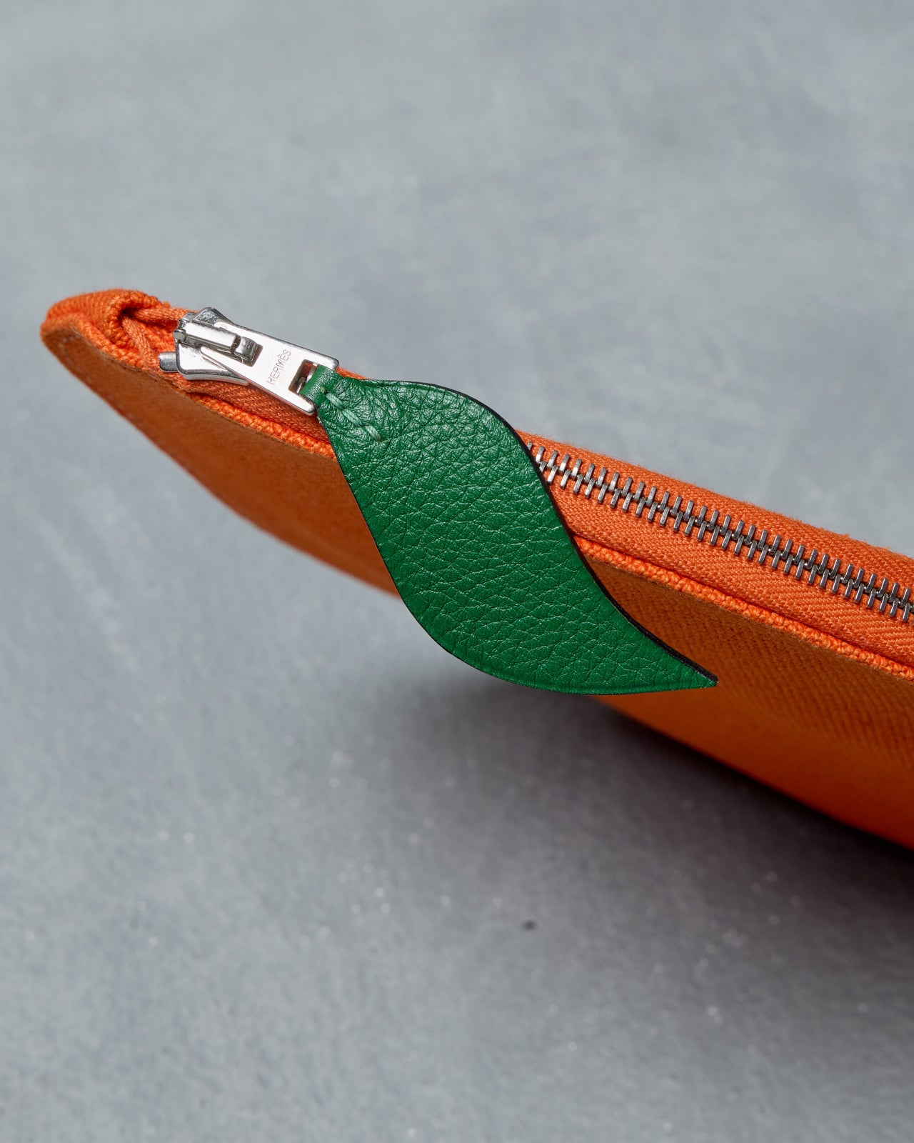 Orange fabric Hermès pouch with a zipper on a gray background