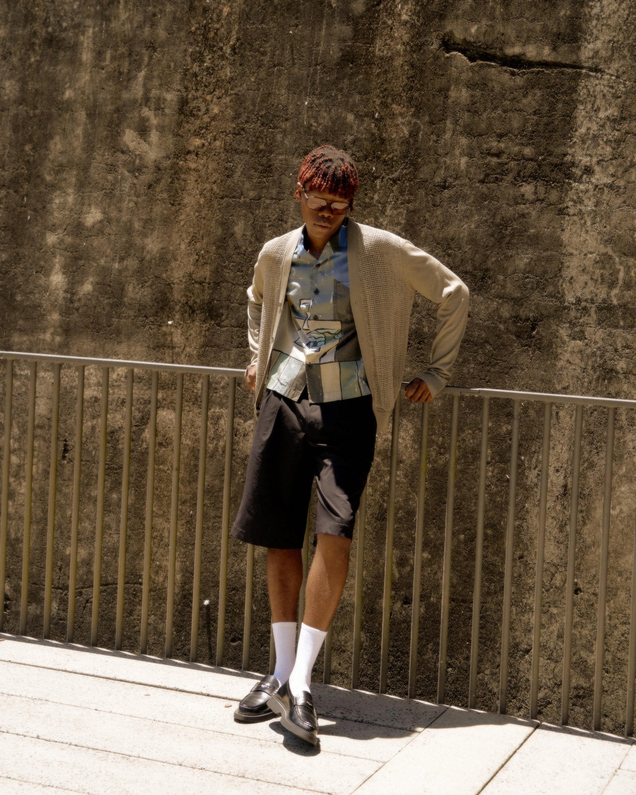 A person standing on a platform wearing a beige woven Hermès cardigan with a round neckline, sleeveless design, and light pants.