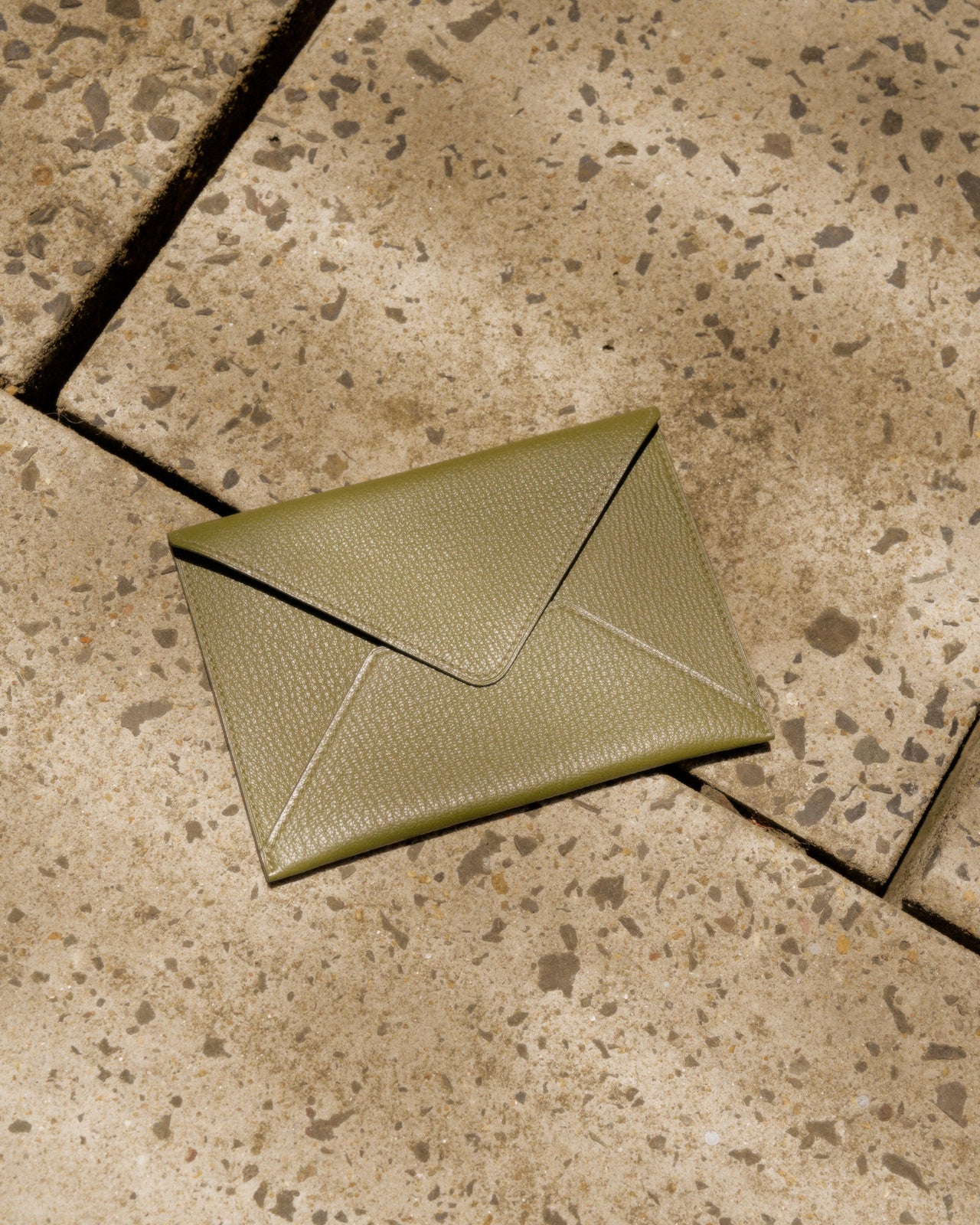 Green Hermès textured envelope-style clutch on speckled stone pavement.