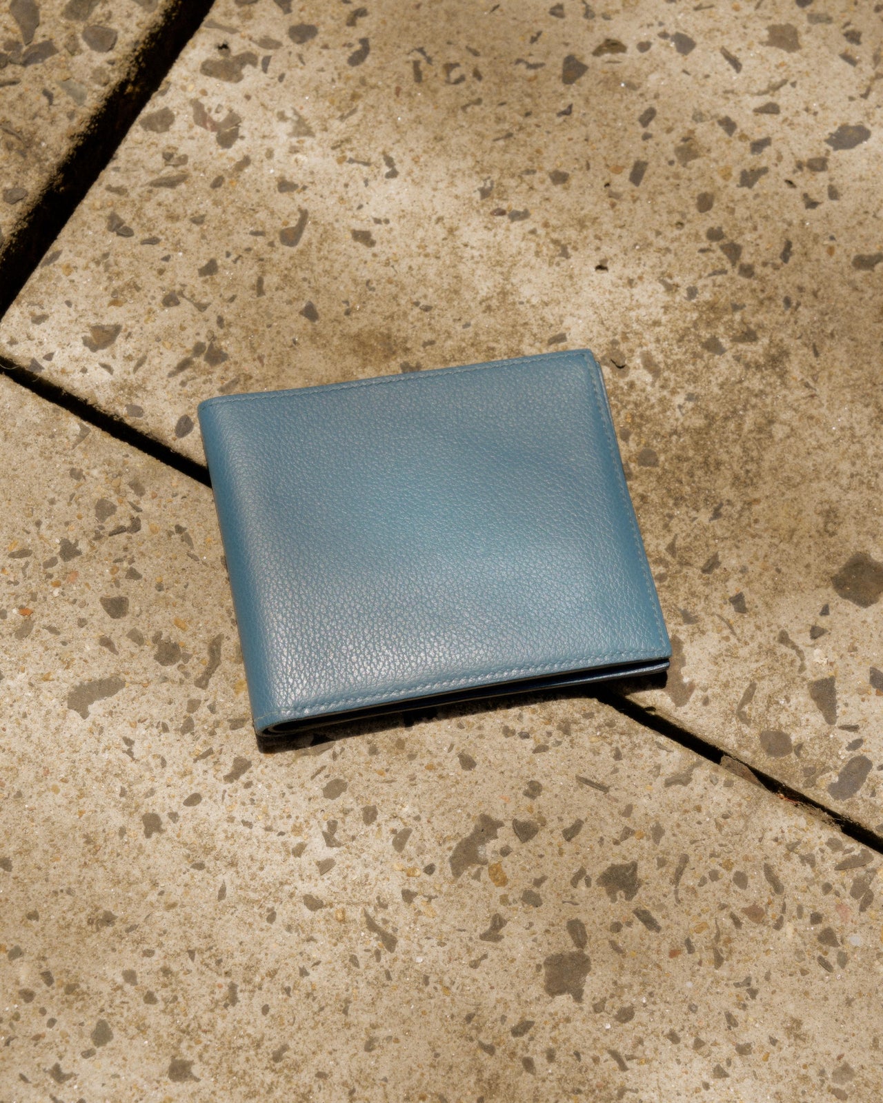 A blue Hermes bifold leather wallet placed on a textured surface.
