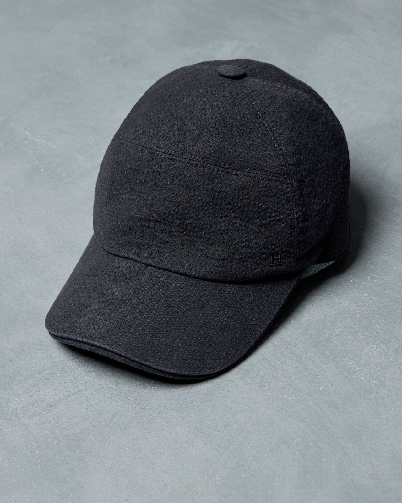 Dark gray Hermès cap on a light gray surface with a gray background