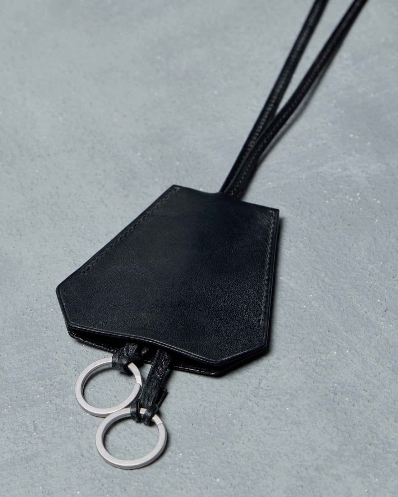 Black Hermes leather keychain necklace with a lanyard on a gray background