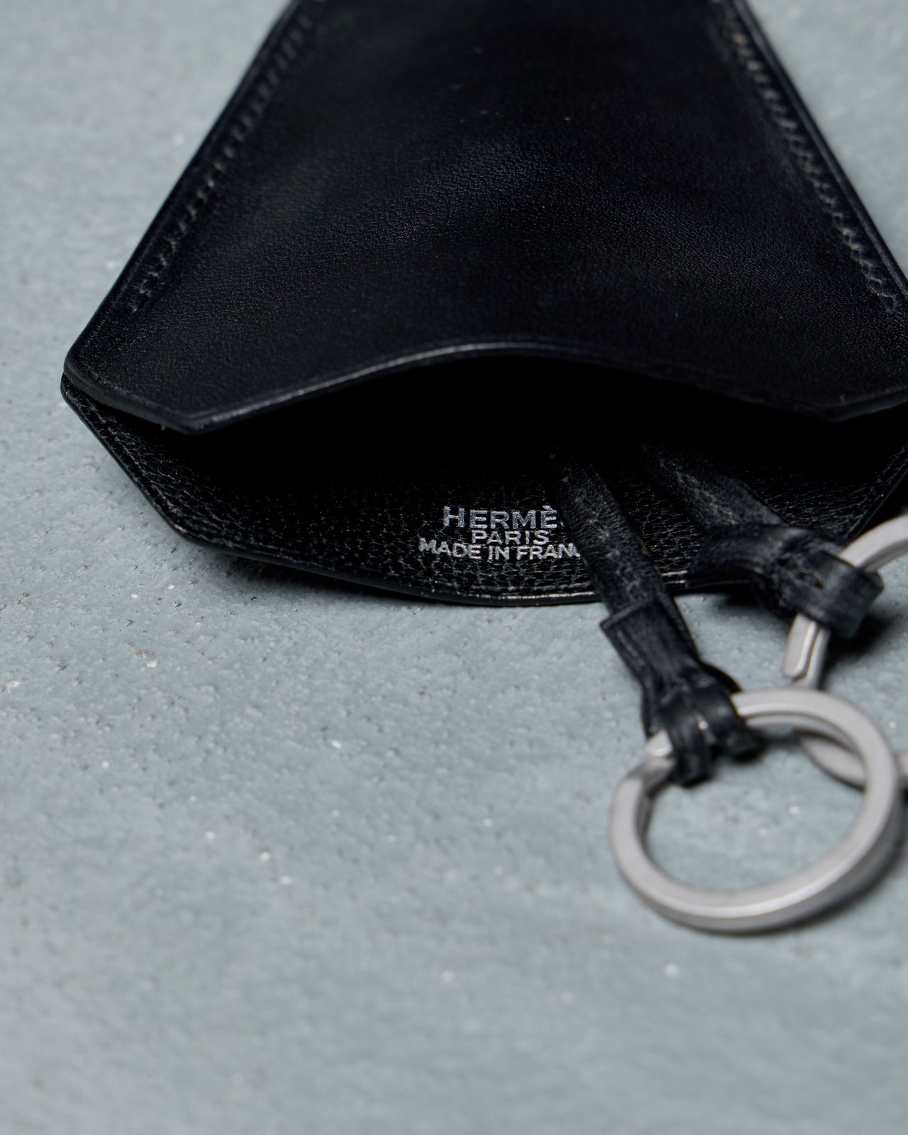 Black Hermes leather keychain necklace with a lanyard on a gray background
