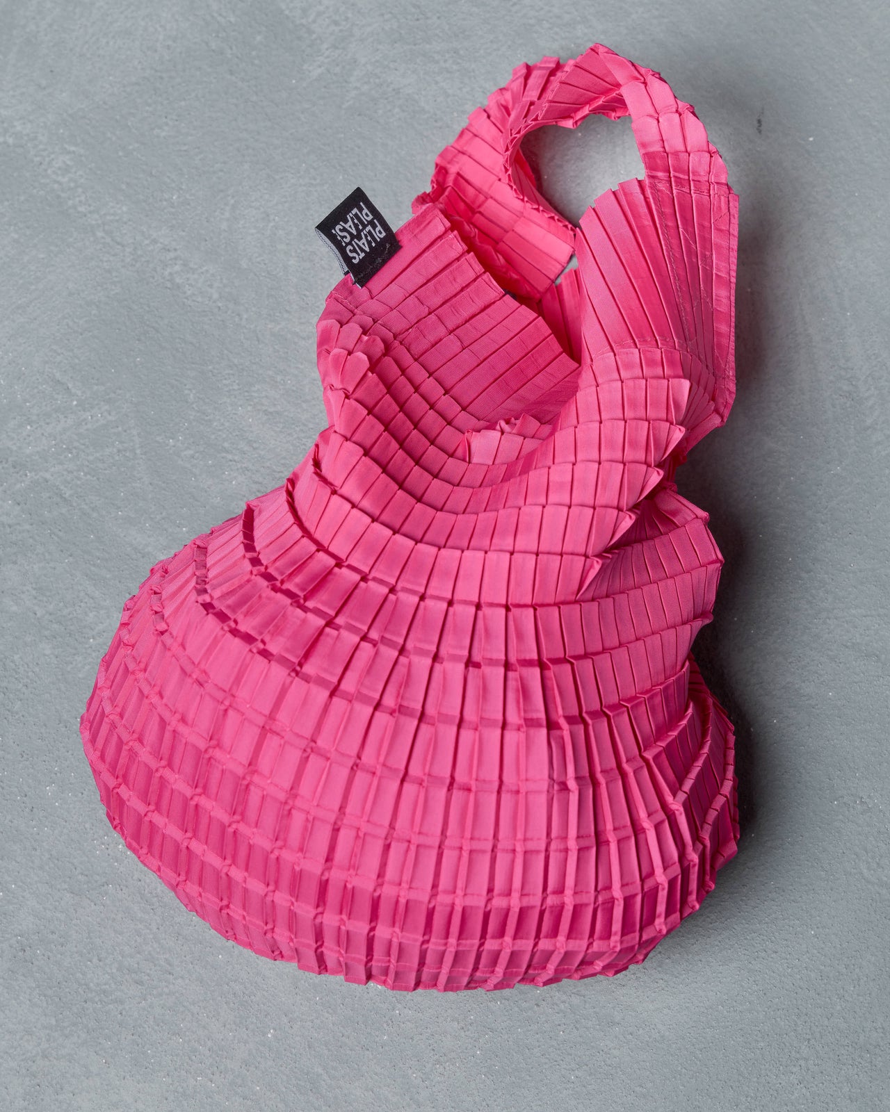 Pink pleated Issey Miyake bag with a brand label on a gray background