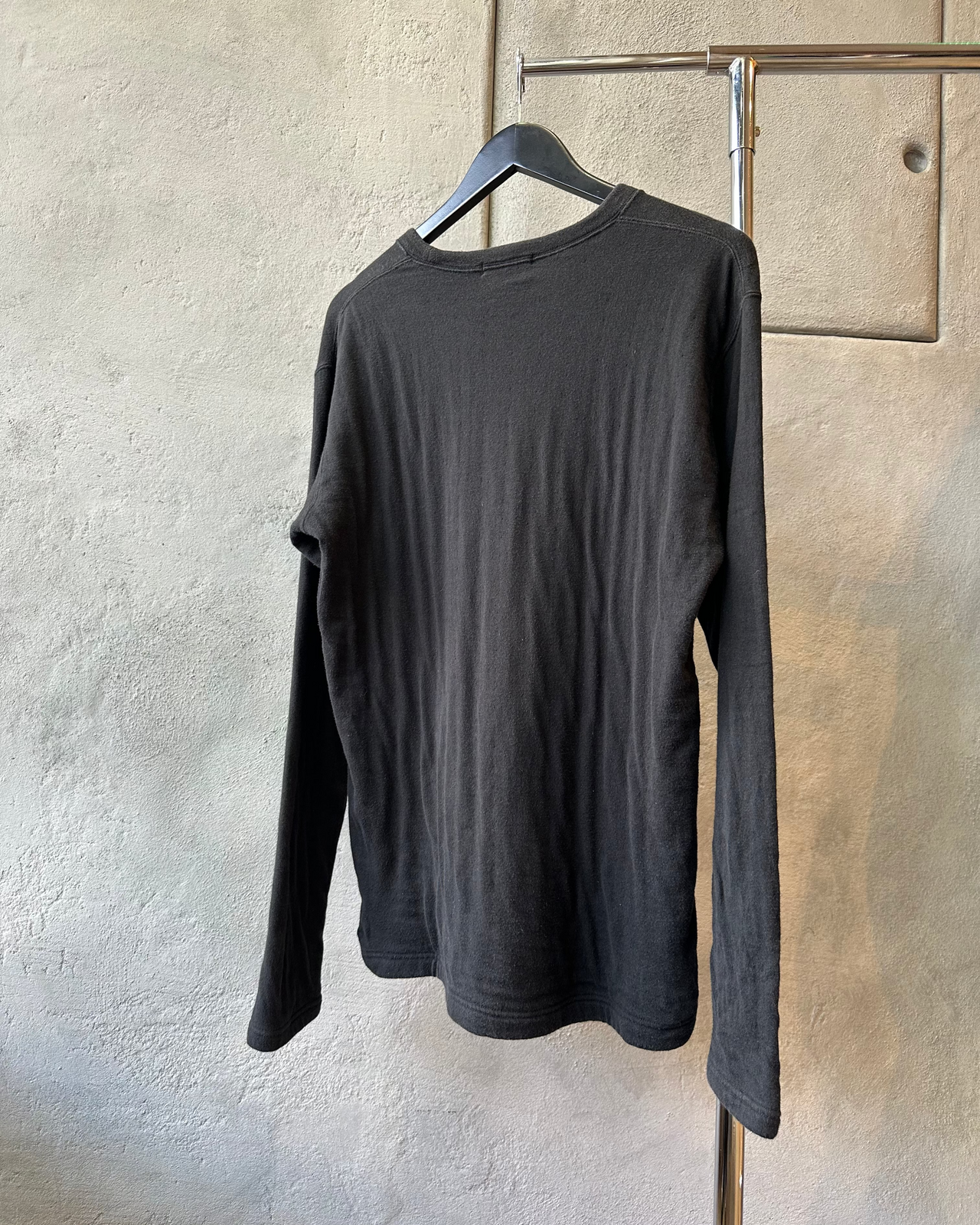 Black long-sleeve Issey Miyake sweater on a hanger against a textured gray wall