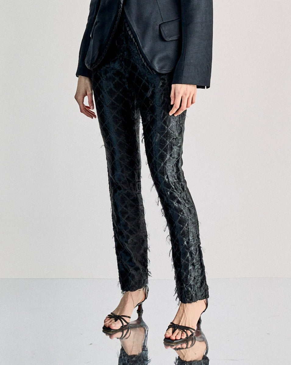 A person wearing black slim-fit JW Anderson trousers with a diamond motif, featuring two side pockets and a straight silhouette, with a zip and button closure.