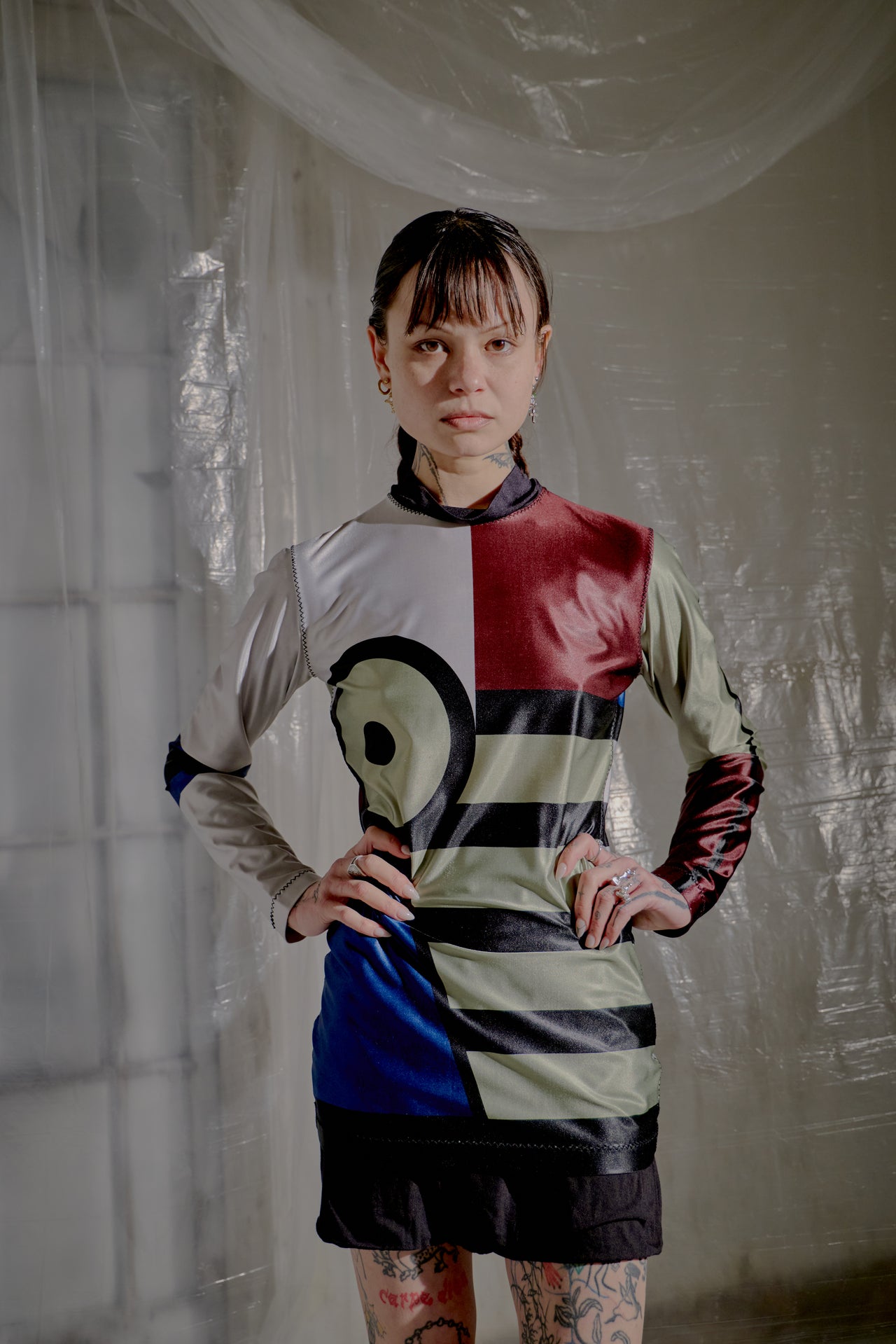 Person wearing a colourful Jean Paul Gaultier top with geometric patterns in a room with reflective white walls.