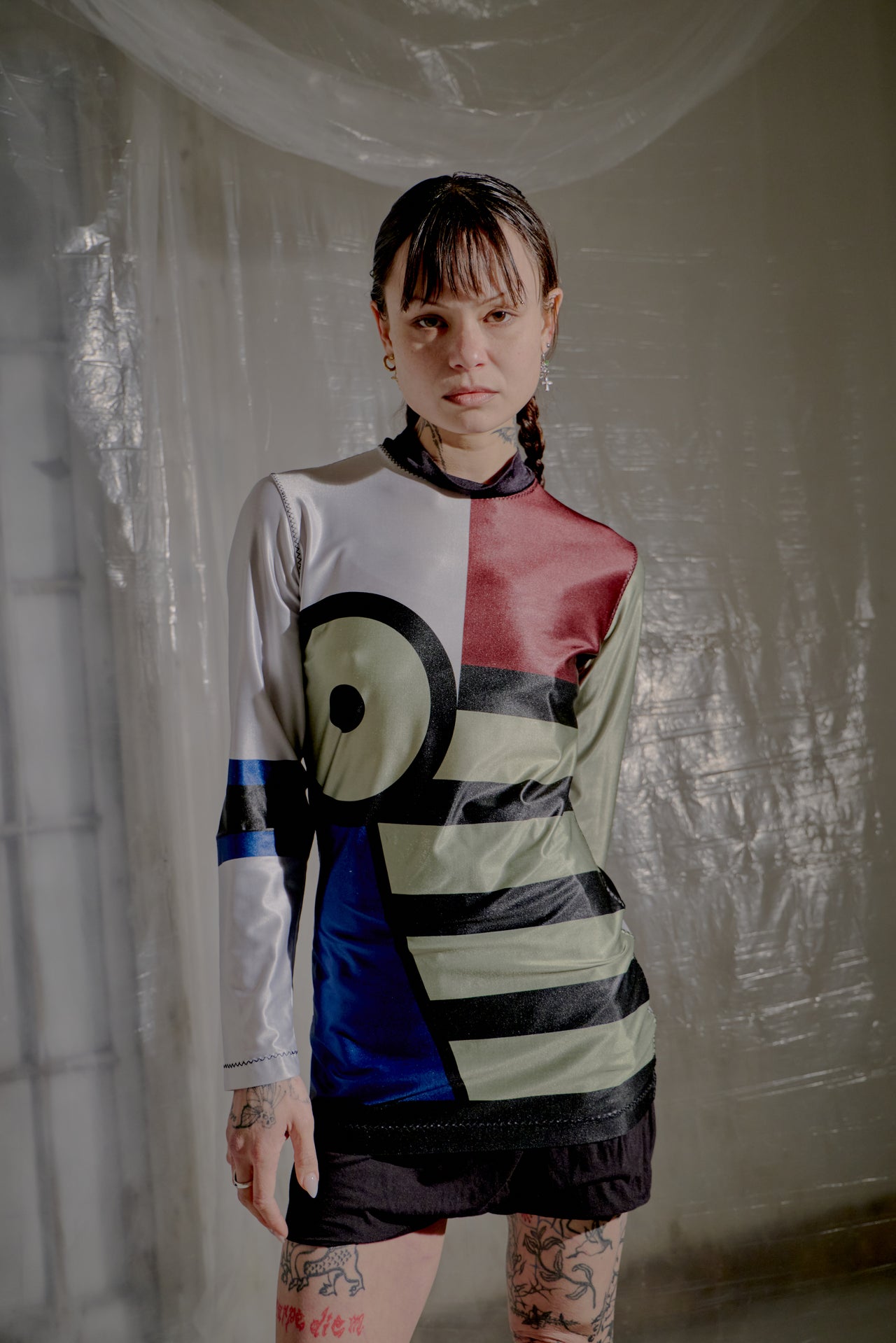 Person wearing a colourful Jean Paul Gaultier top with geometric patterns in a room with reflective white walls.