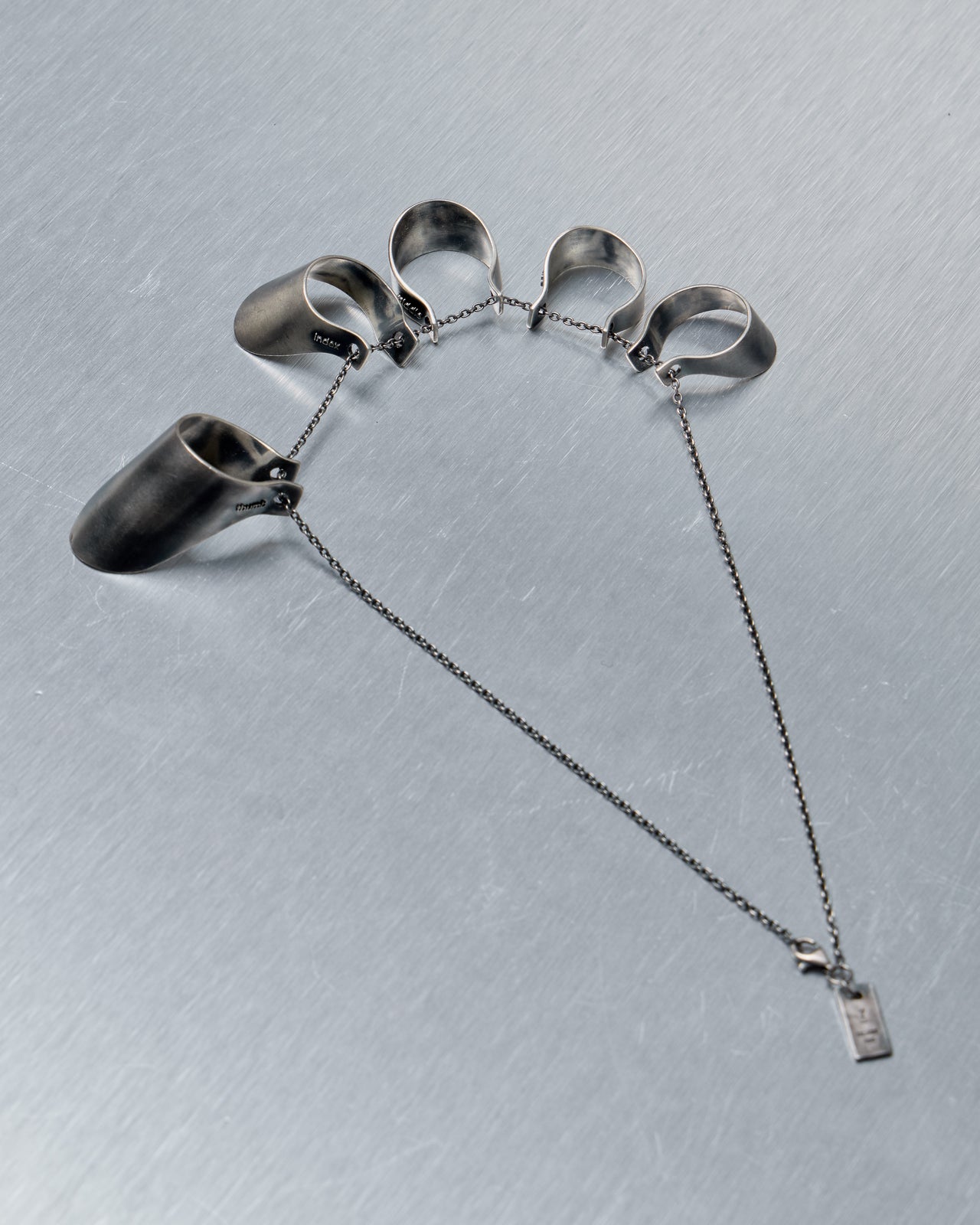 Silver necklace from Julius with five finger rings on a gray background