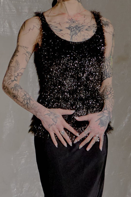 Person in a black dress standing in a room with white fabric and brick walls.