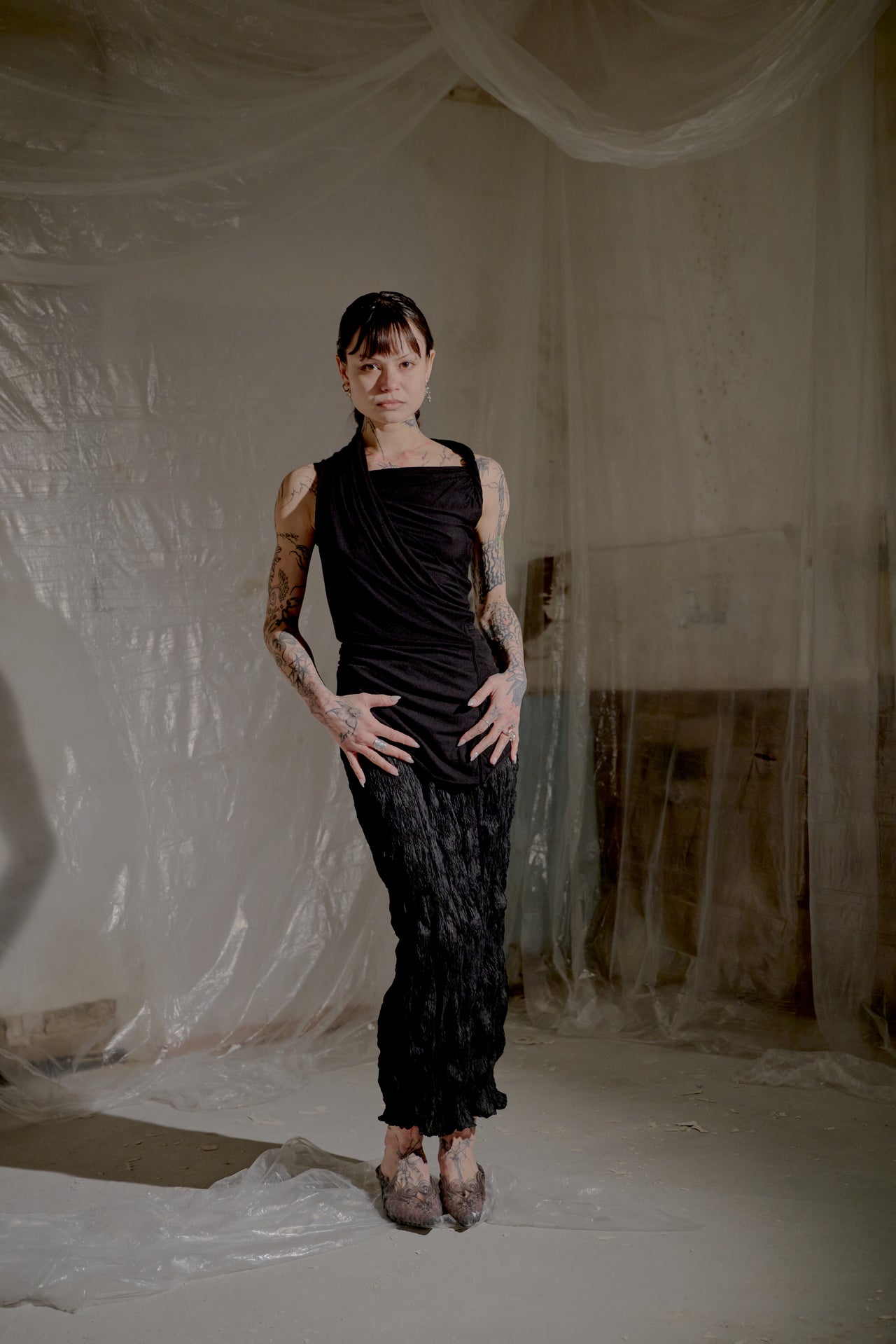 Person wearing a black sleeveless top and pants in a room with white draped fabric.