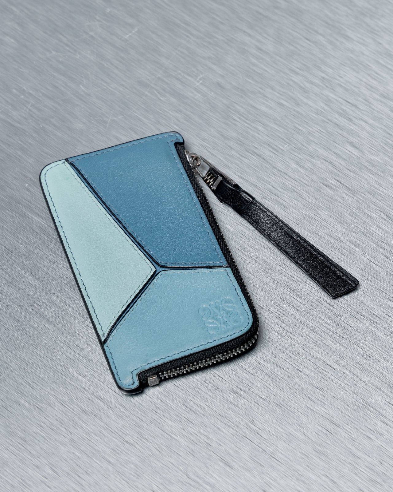 Blue and black Loewe puzzle wallet with a strap on a gray textured surface