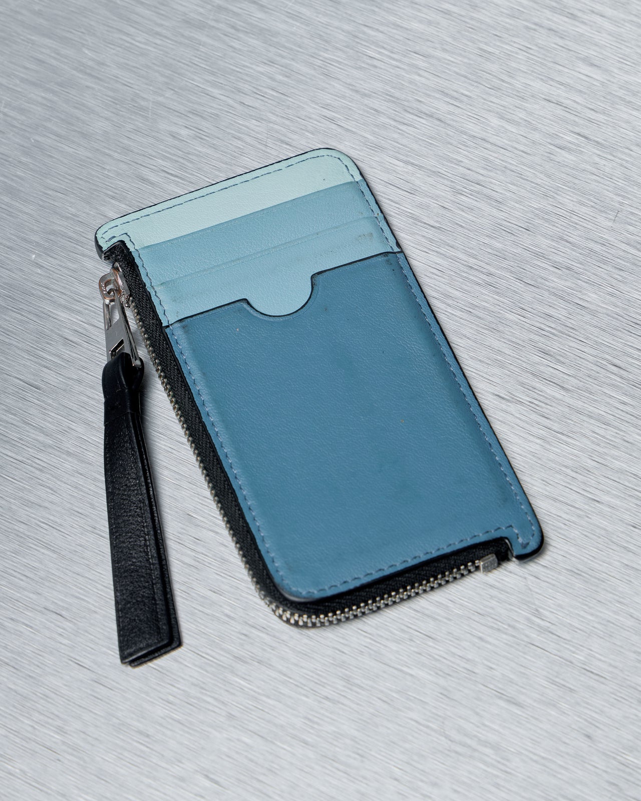 Blue and black Loewe puzzle wallet with a strap on a gray textured surface