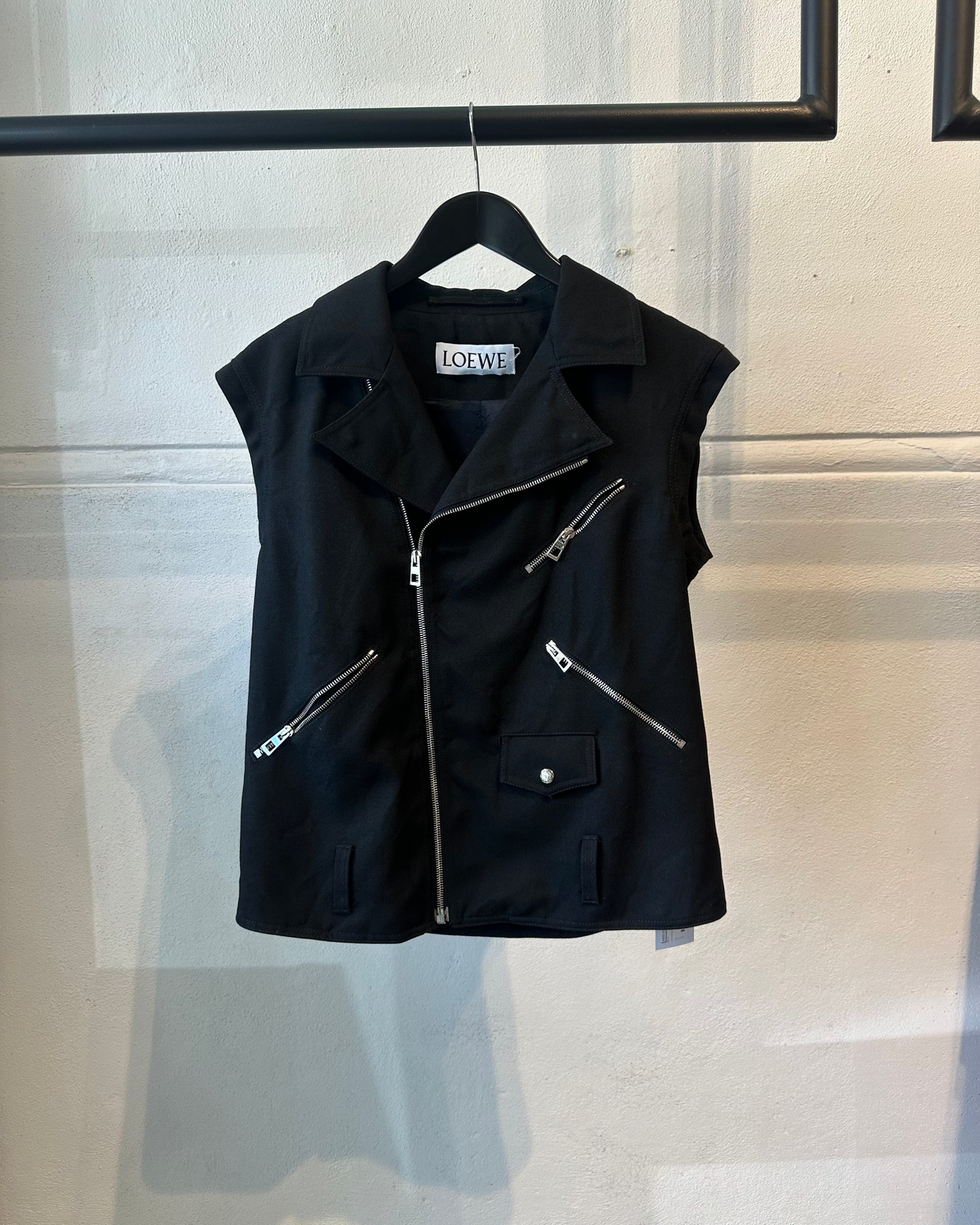 Black Loewe vest with zippers on a hanger against a neutral background