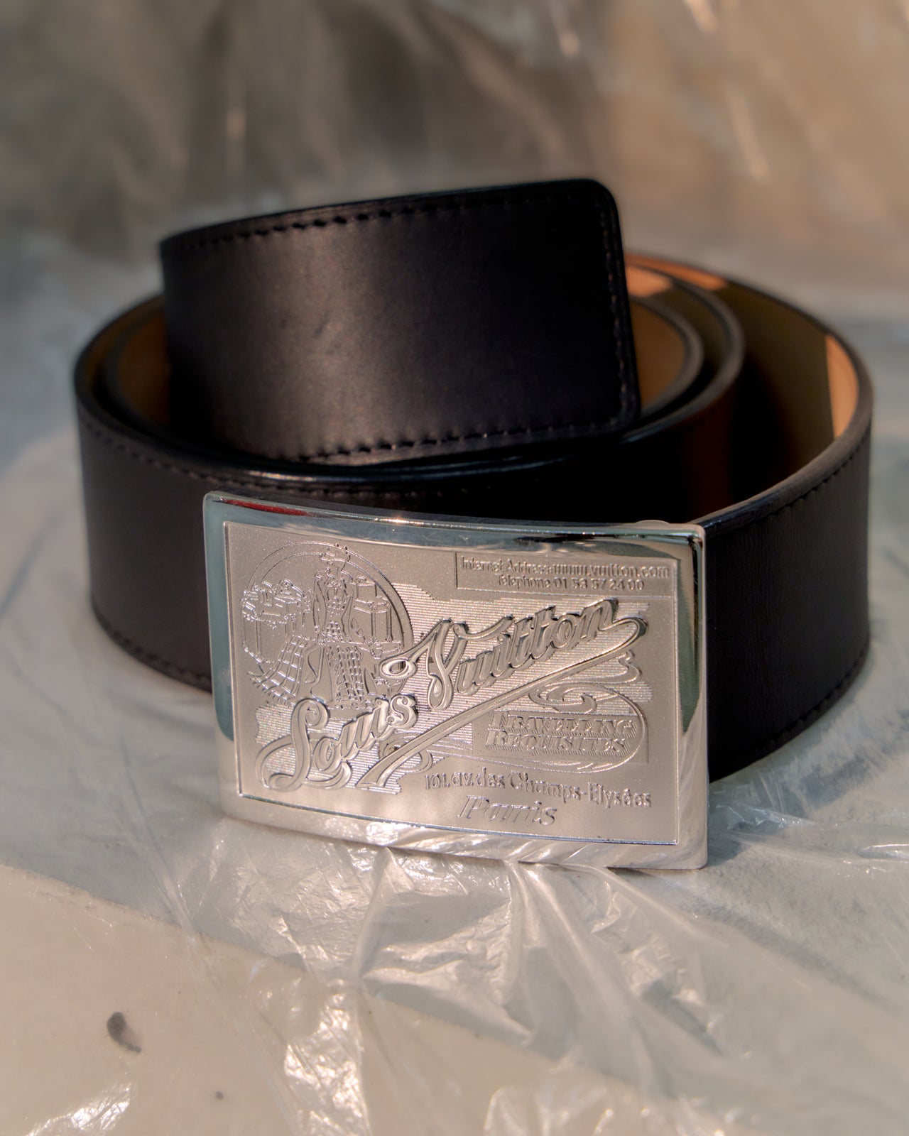 Black Louis Vuitton belt with a silver buckle on a reflective surface