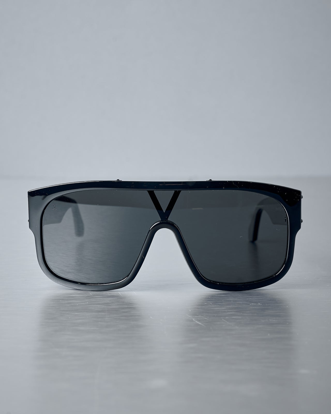 Black Louis Vuitton sunglasses with a reflective surface on a grey background