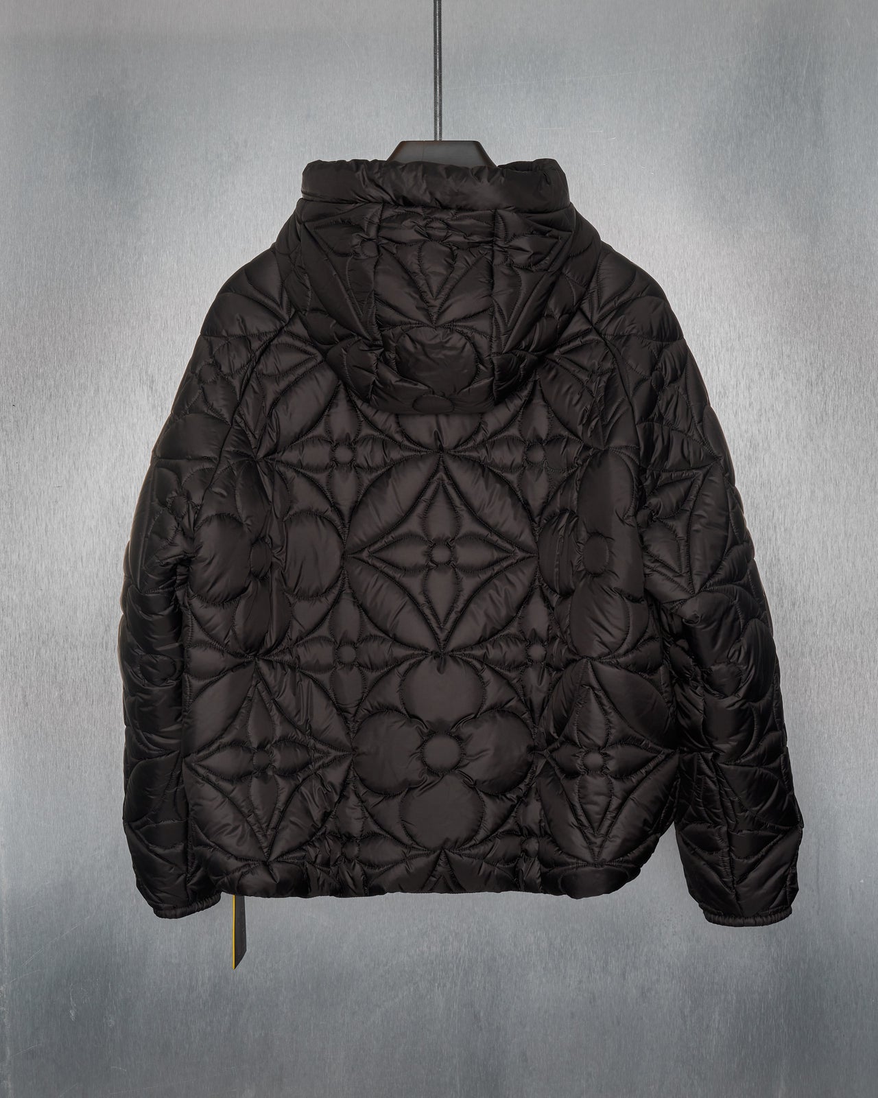 A black Louis Vuitton quilted hoodie jacket with LVSE flower quilting, featuring a hood, zippered closures, and padded cuffs.