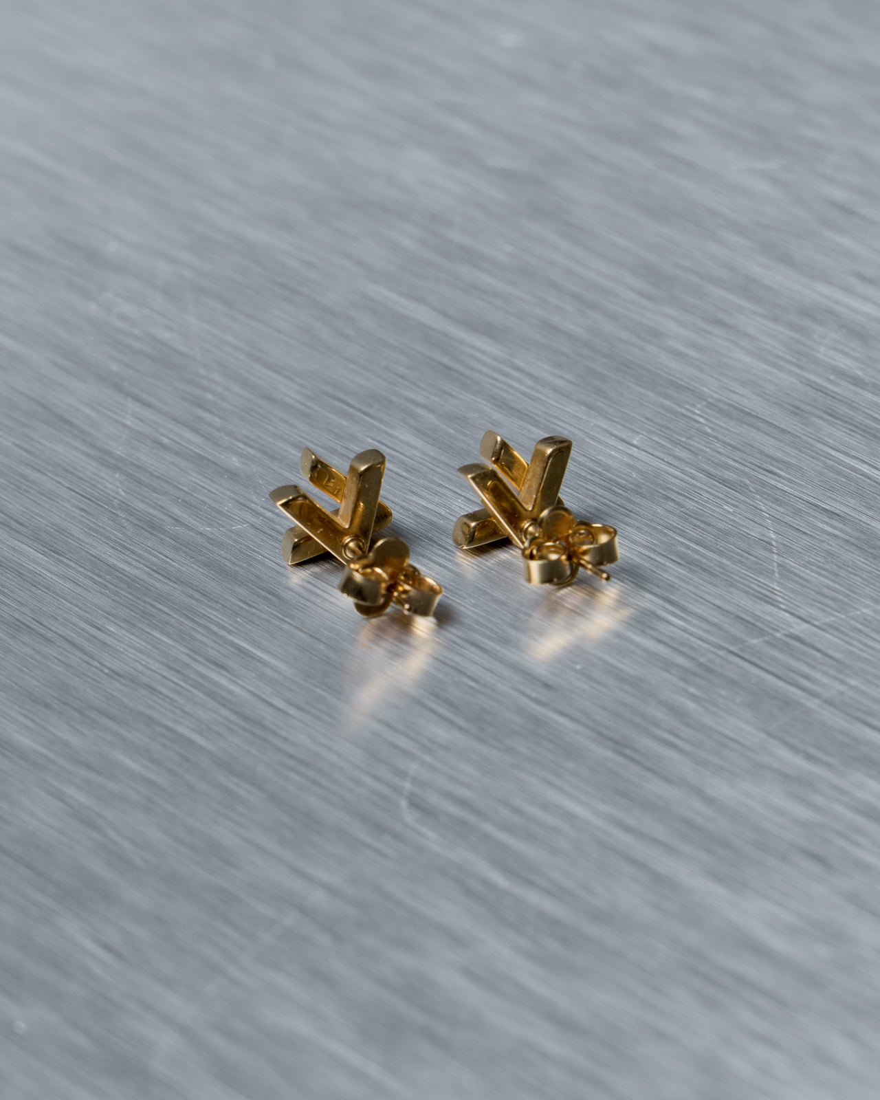 Pair of gold Louis Vuitton earrings on a textured gray surface