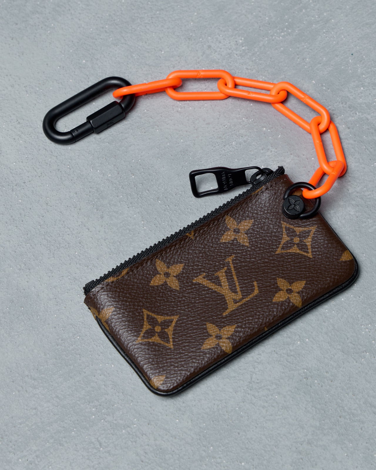 Louis Vuitton key pouch with orange chain and black carabiner on a gray background