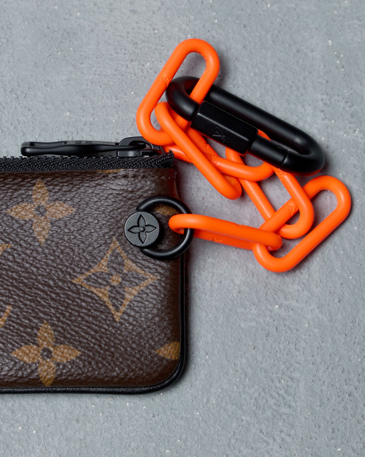 Louis Vuitton key pouch with orange chain and black carabiner on a gray background