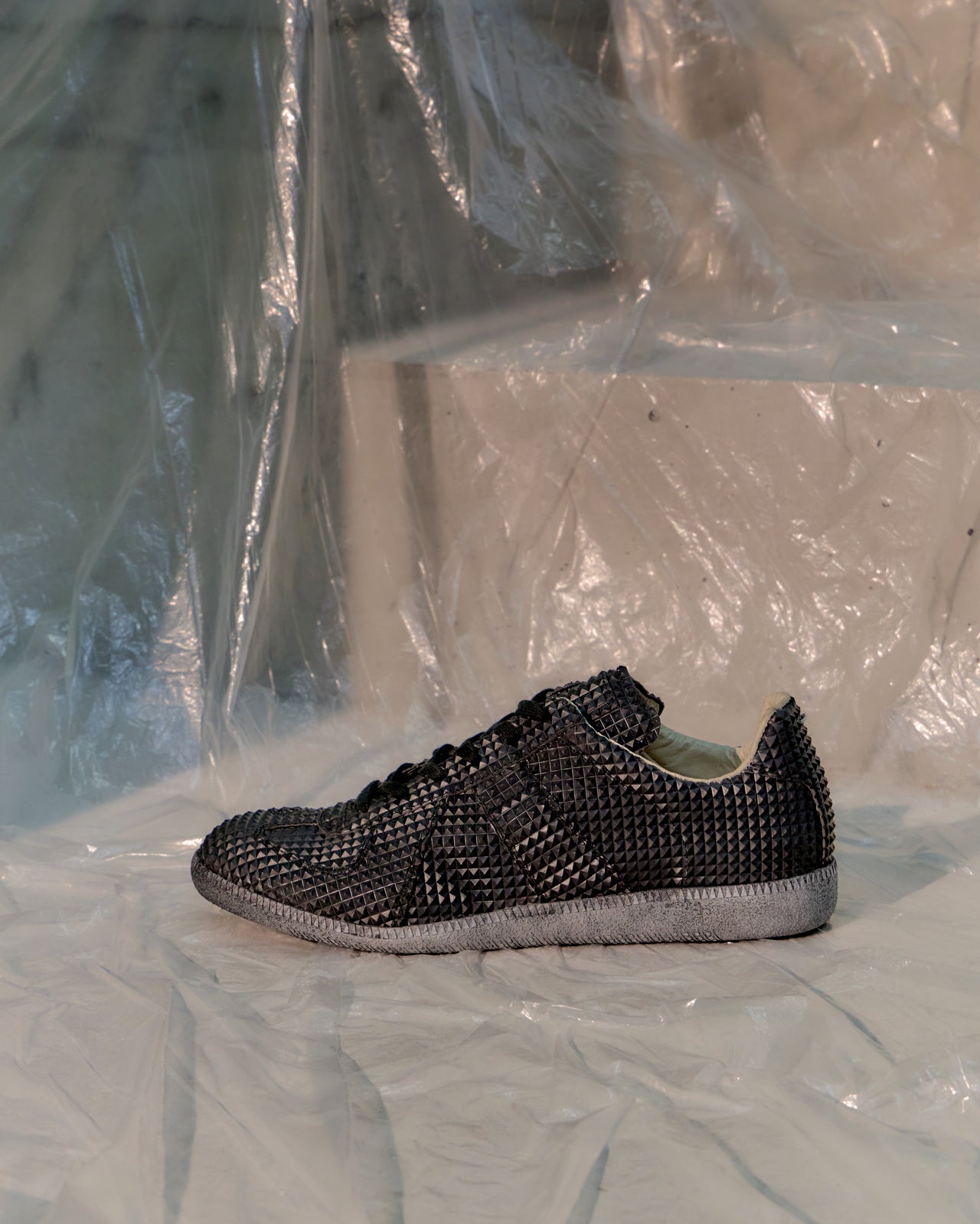 Black textured Maison Margiela GAT sneaker on a white surface with a plastic sheet background