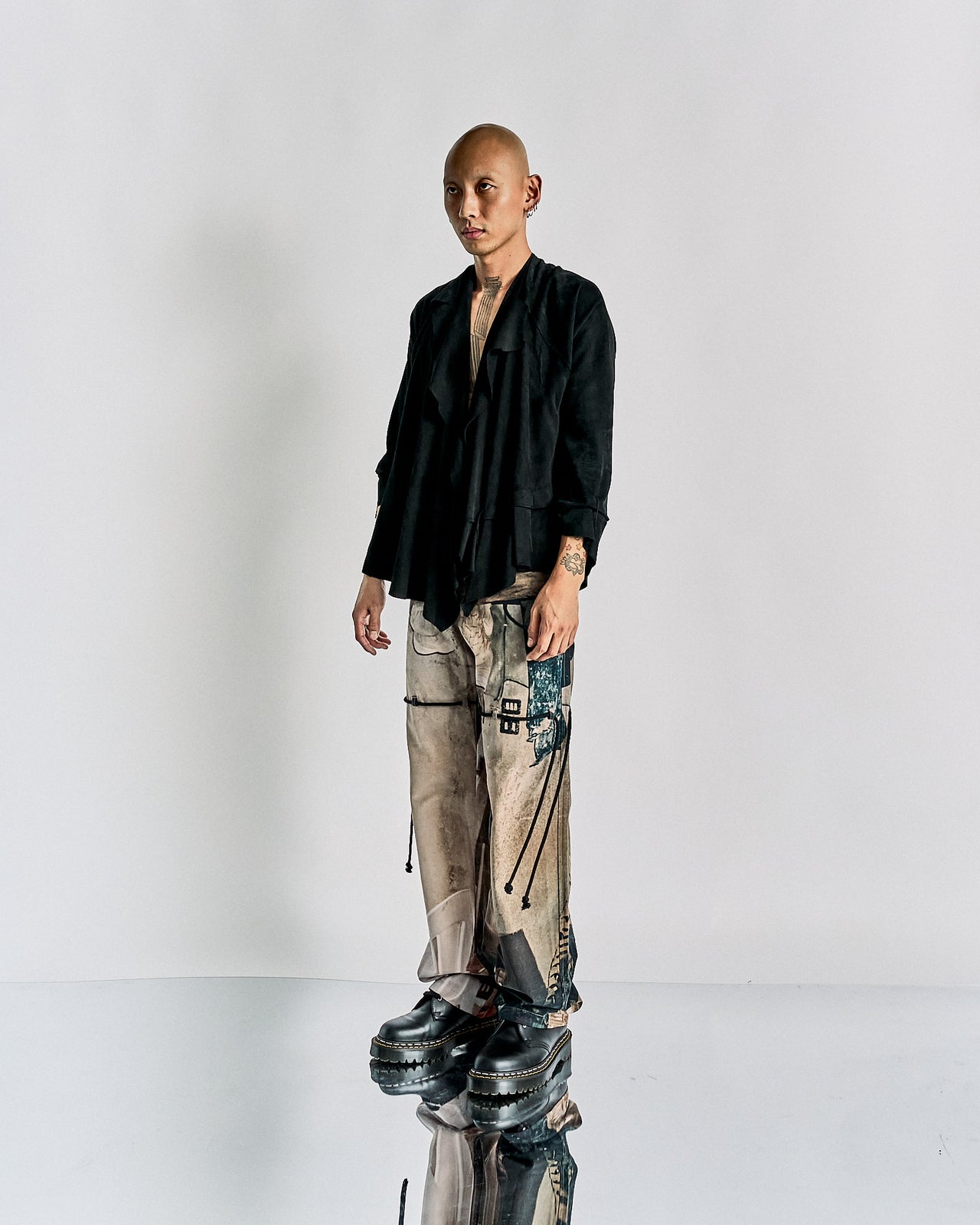 A person wearing a black Maison Margiela jacket and pants with an irregular patchwork suede jacket design.